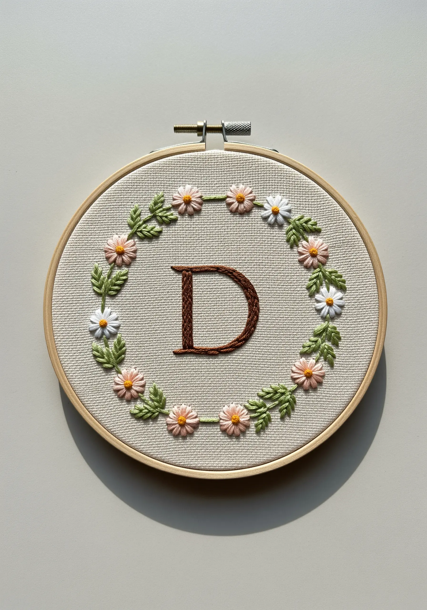 A brown initial 'D' surrounded by a delicate wreath of embroidered daisies.