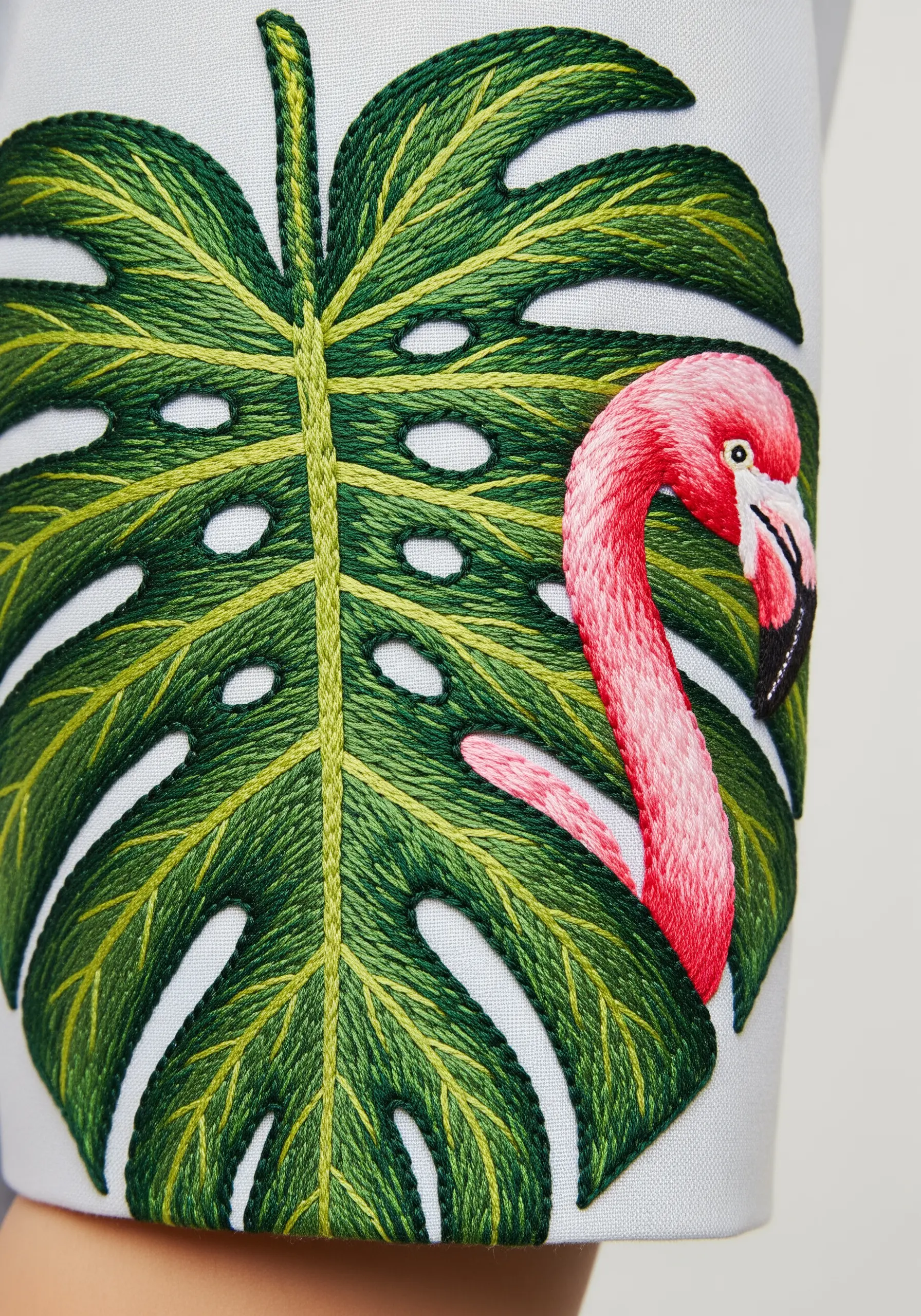 A pink flamingo head peeking through a large, detailed green embroidered monstera leaf.