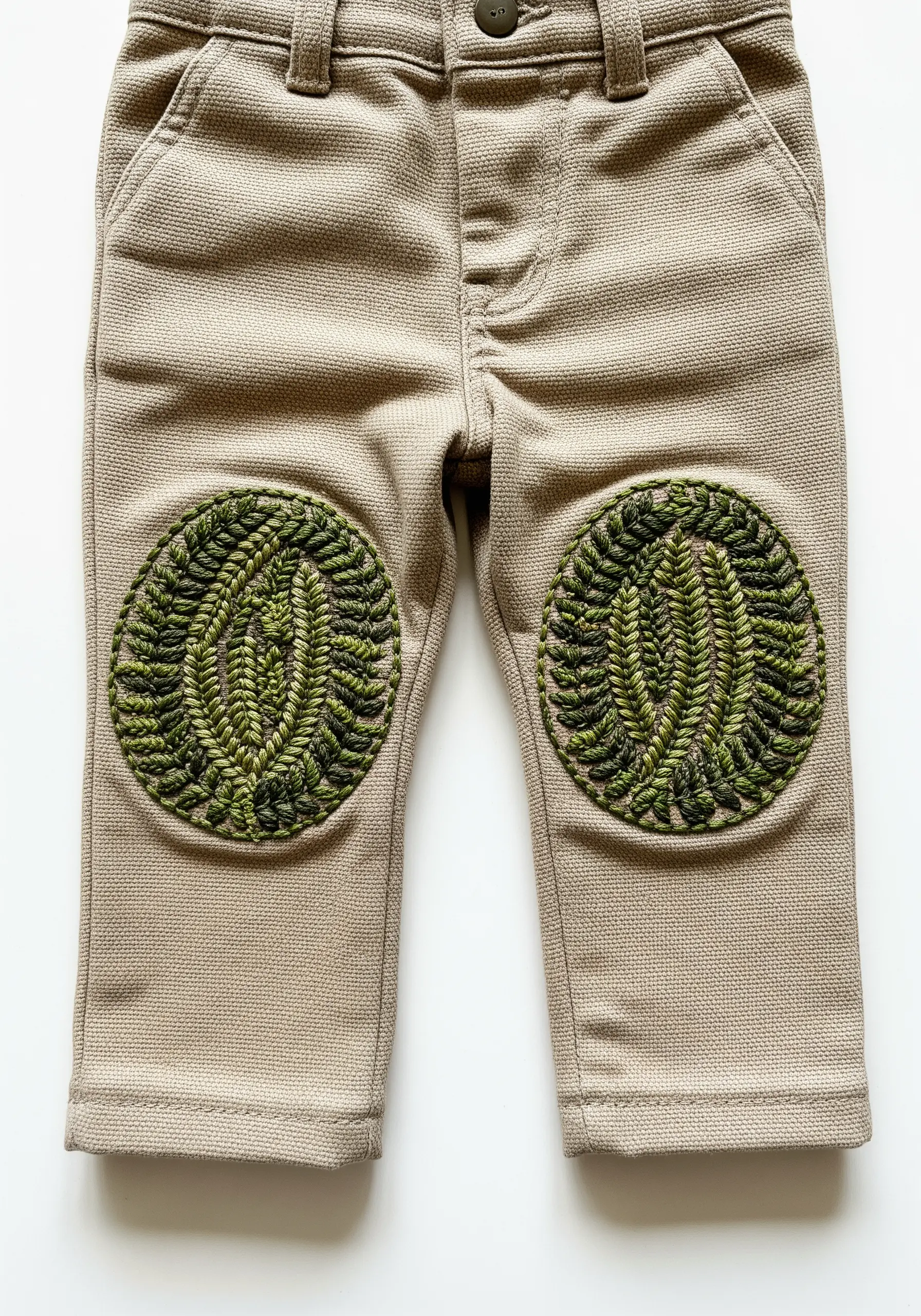 Circular knee patches on toddler pants, densely embroidered with fern leaf patterns.