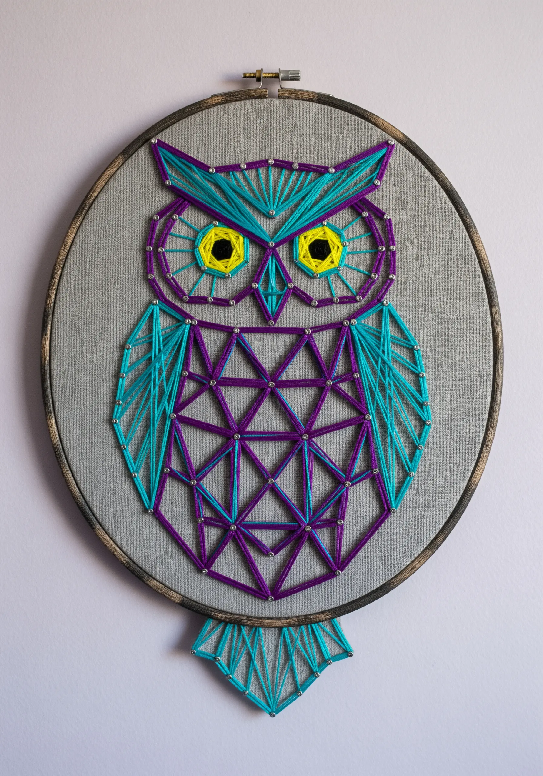 A stylized geometric owl embroidered in purple and teal with bright yellow eyes.