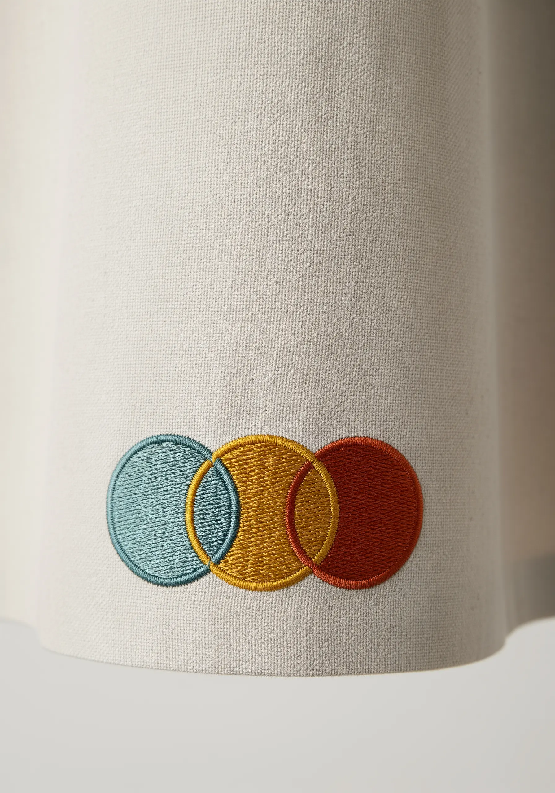 Three overlapping satin stitch circles in blue, yellow, and red on a cream fabric.