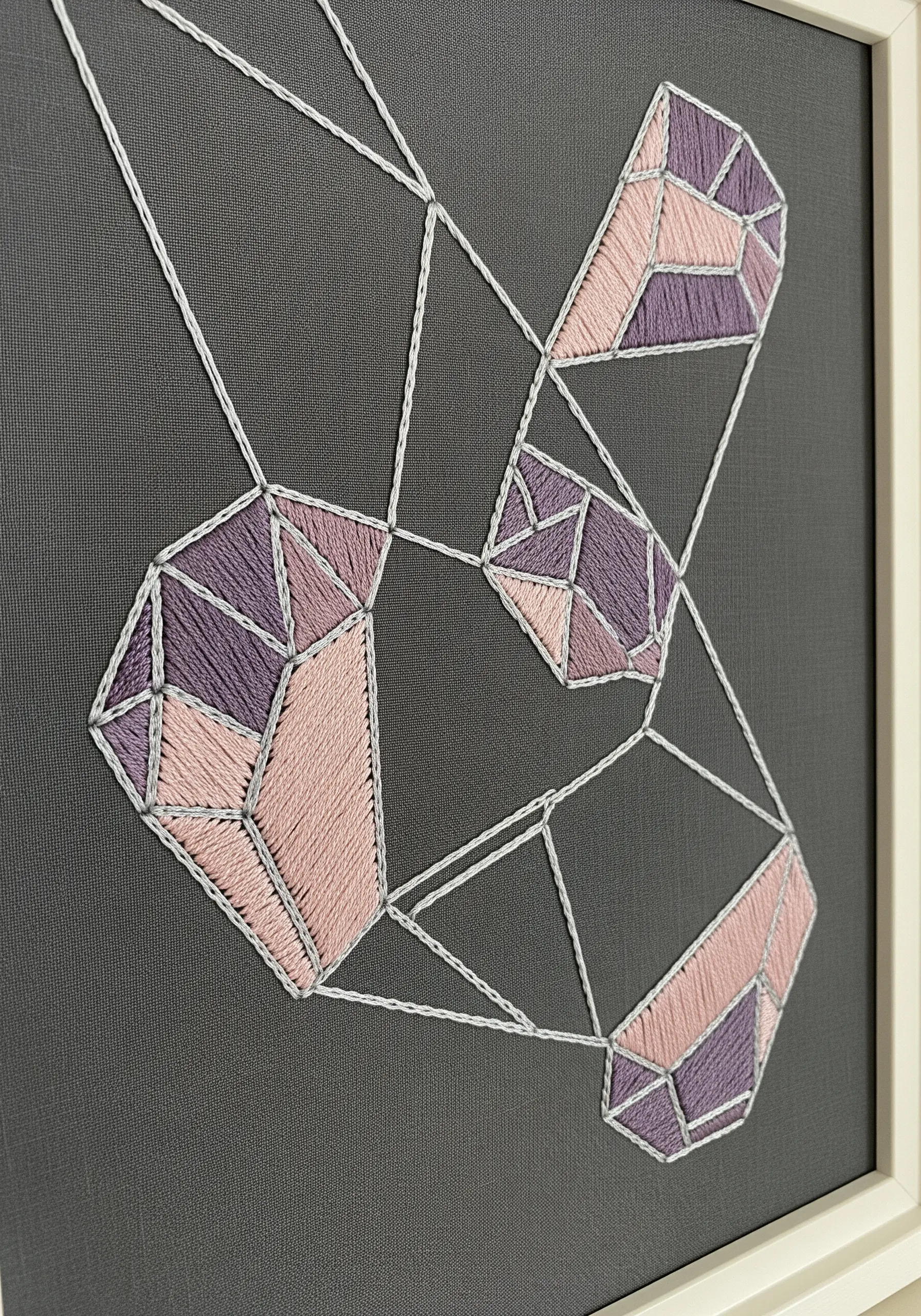Close-up of geometric gem shapes embroidered with pink and purple satin stitch on dark grey fabric.