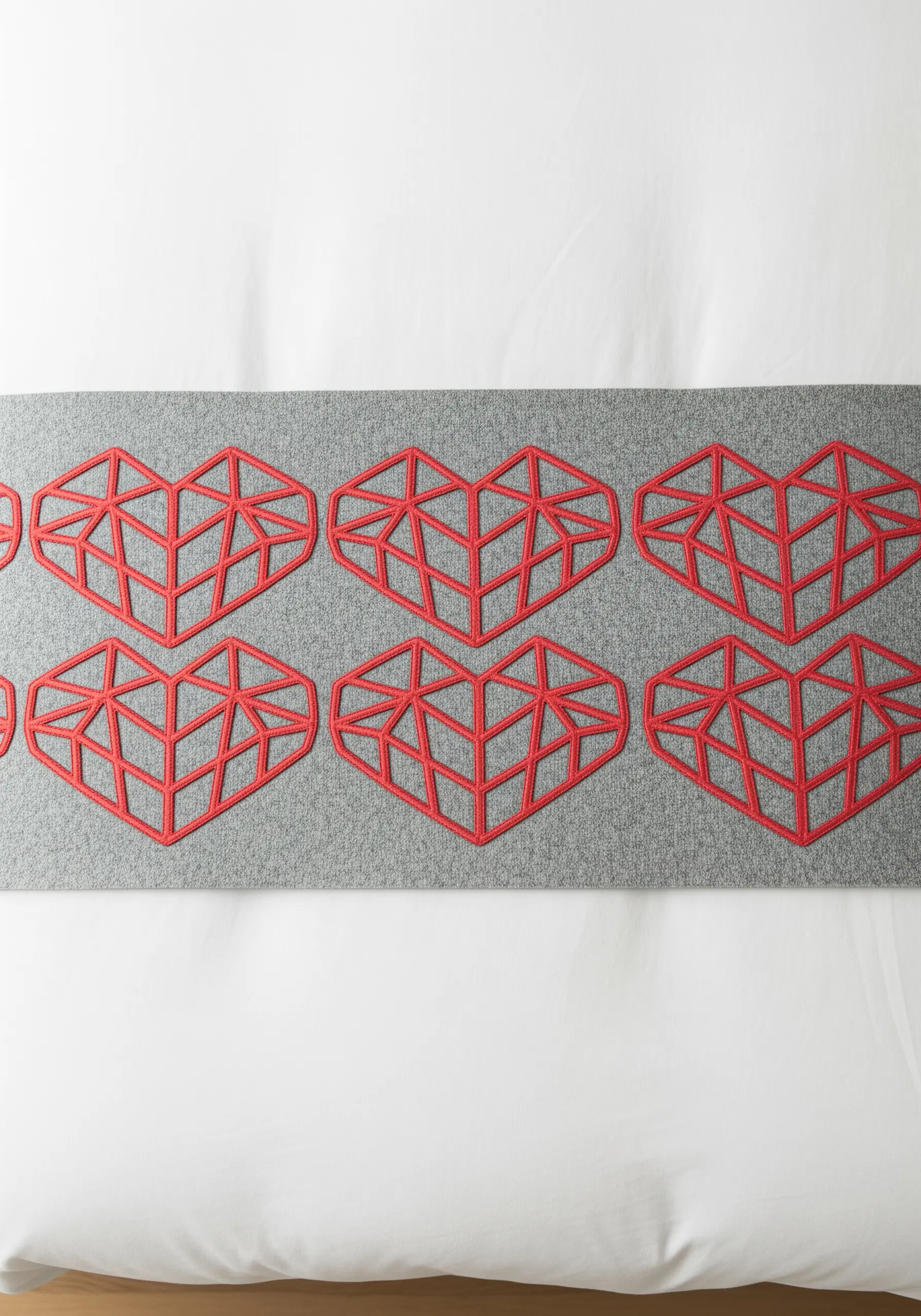 A pattern of geometric, linear red hearts embroidered on a grey bed runner.