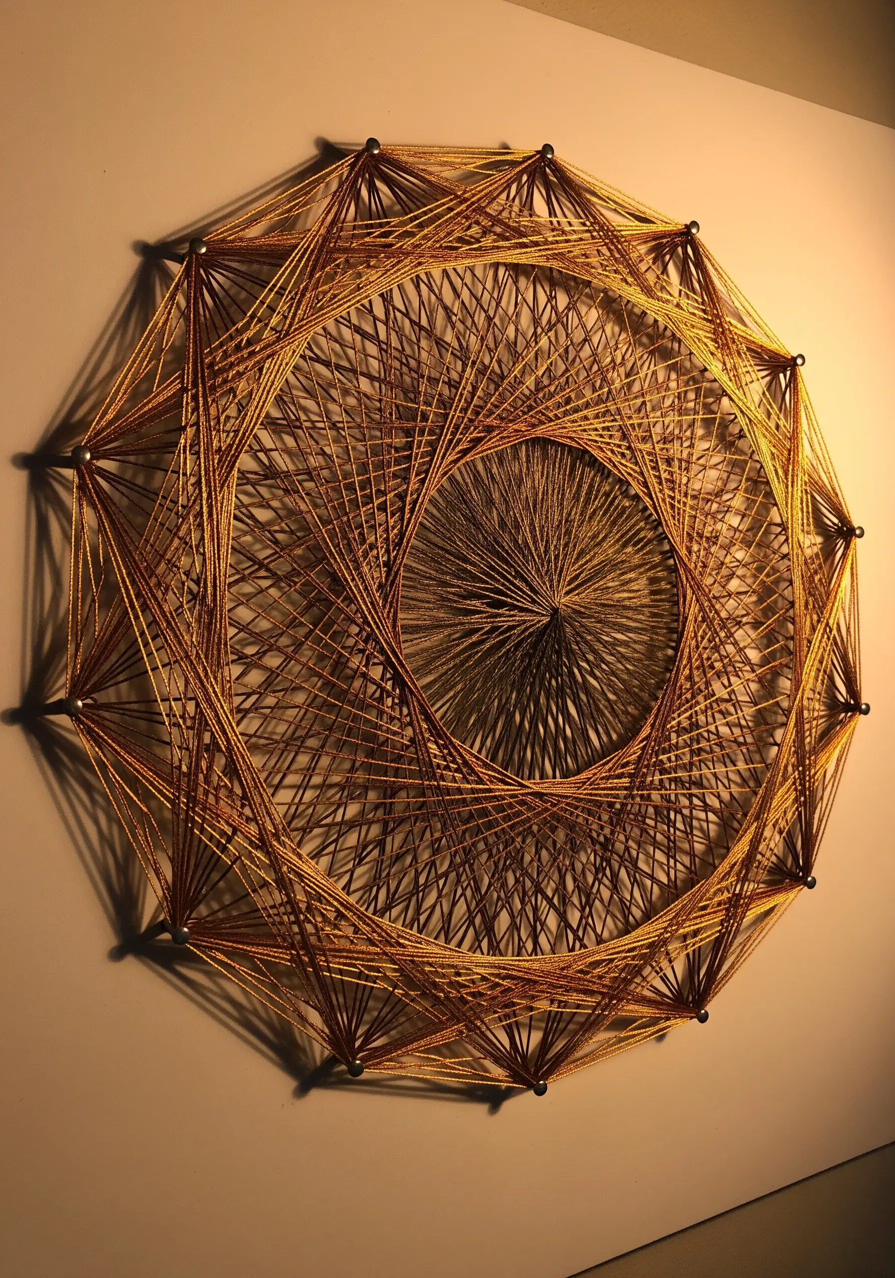 Geometric string art made with gold metallic thread, creating a lightburst effect.