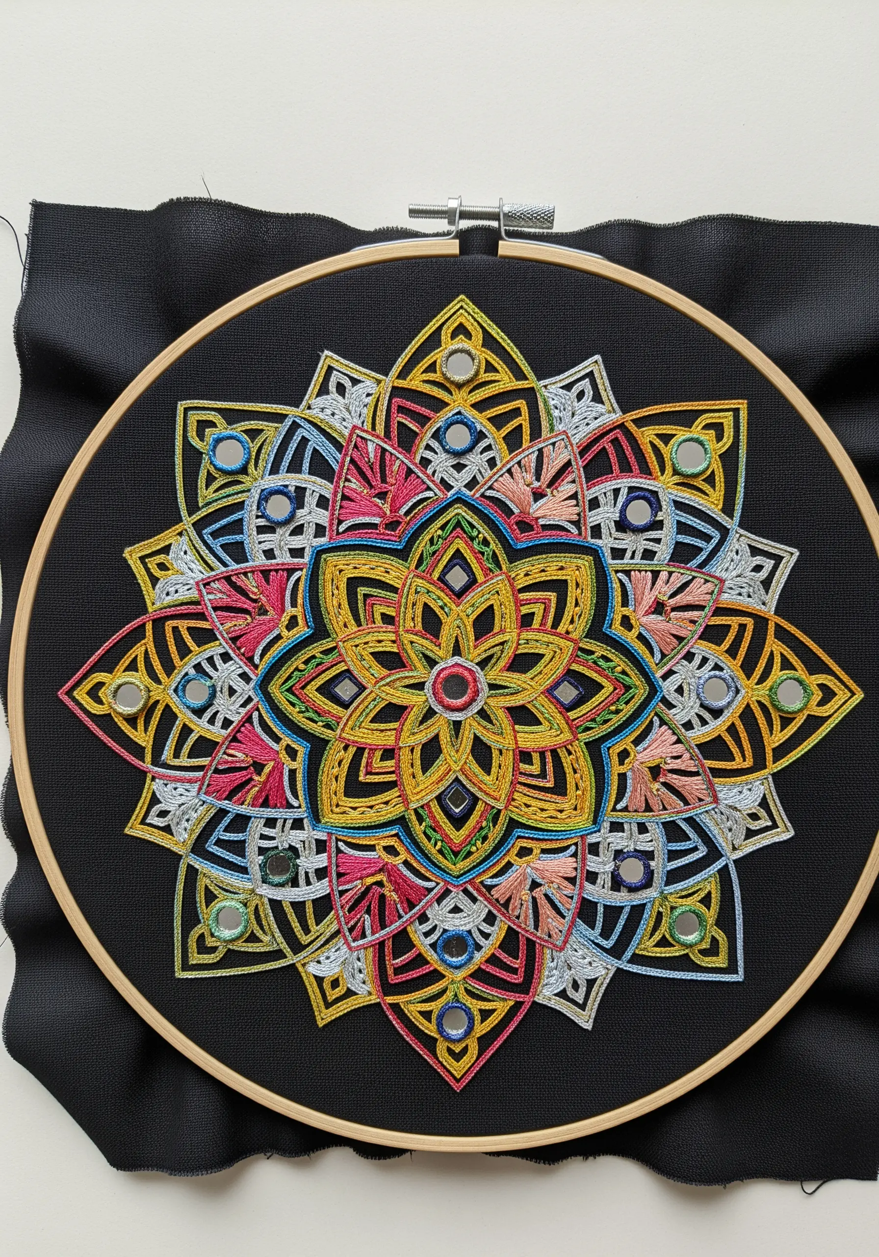 A colorful geometric mandala stitched on black fabric, with small, round shisha mirrors integrated.