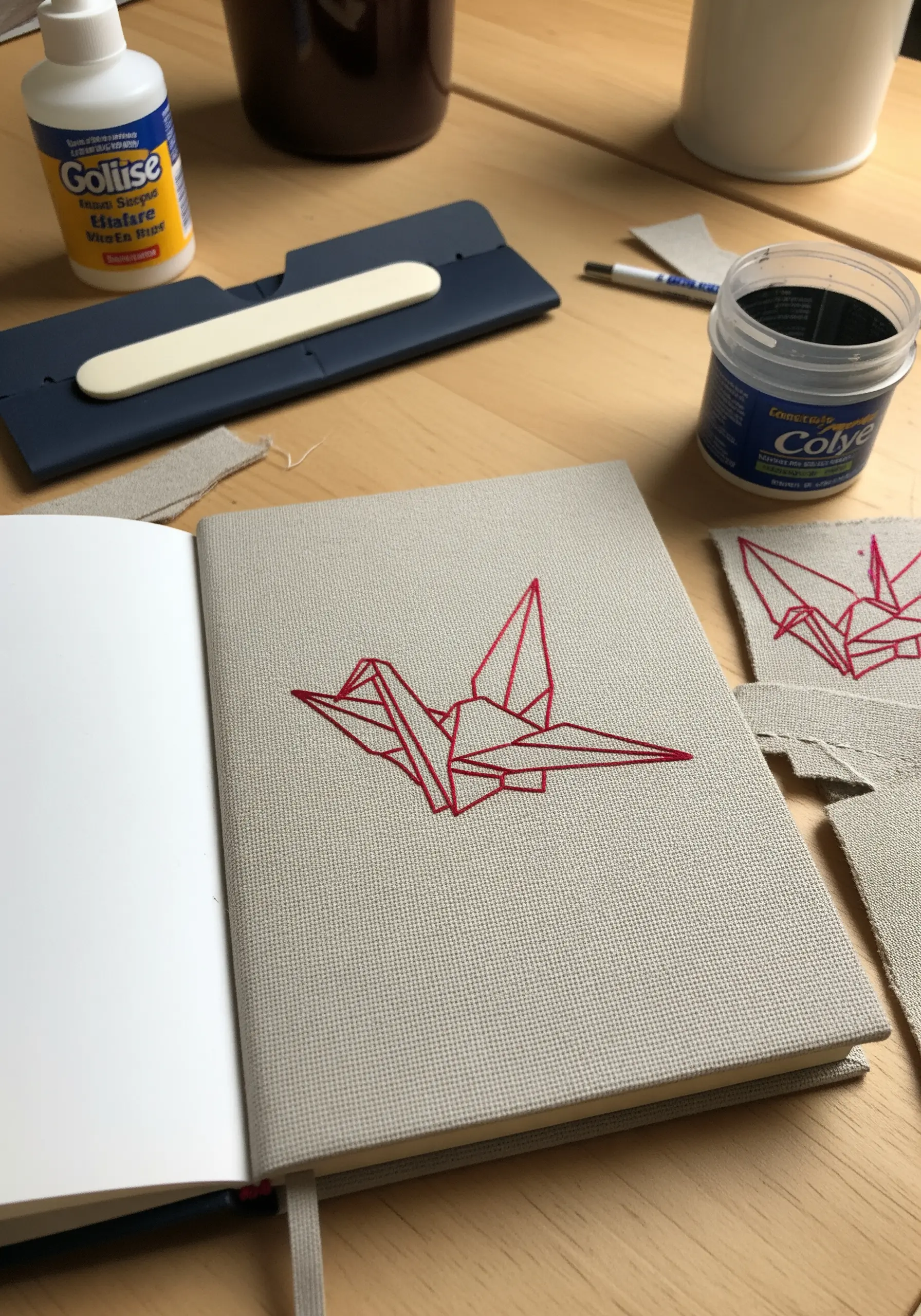 A red thread geometric origami crane embroidered on the cover of a fabric journal.
