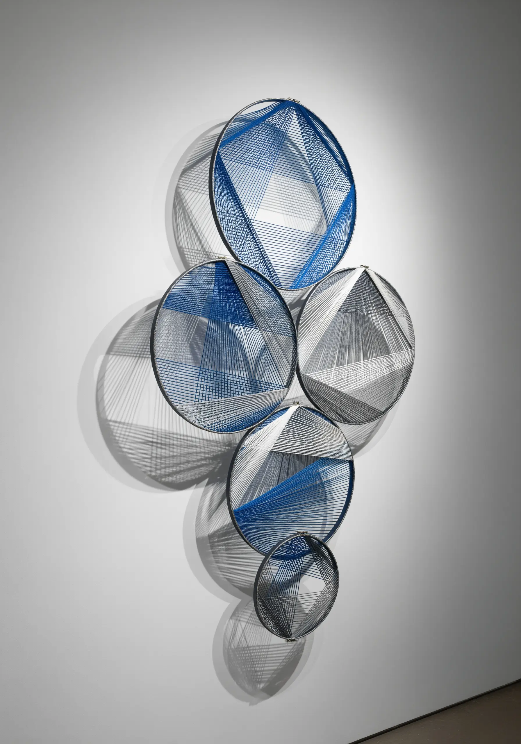 Layered blue and grey threads creating geometric patterns and shadows within five stacked metal hoops.