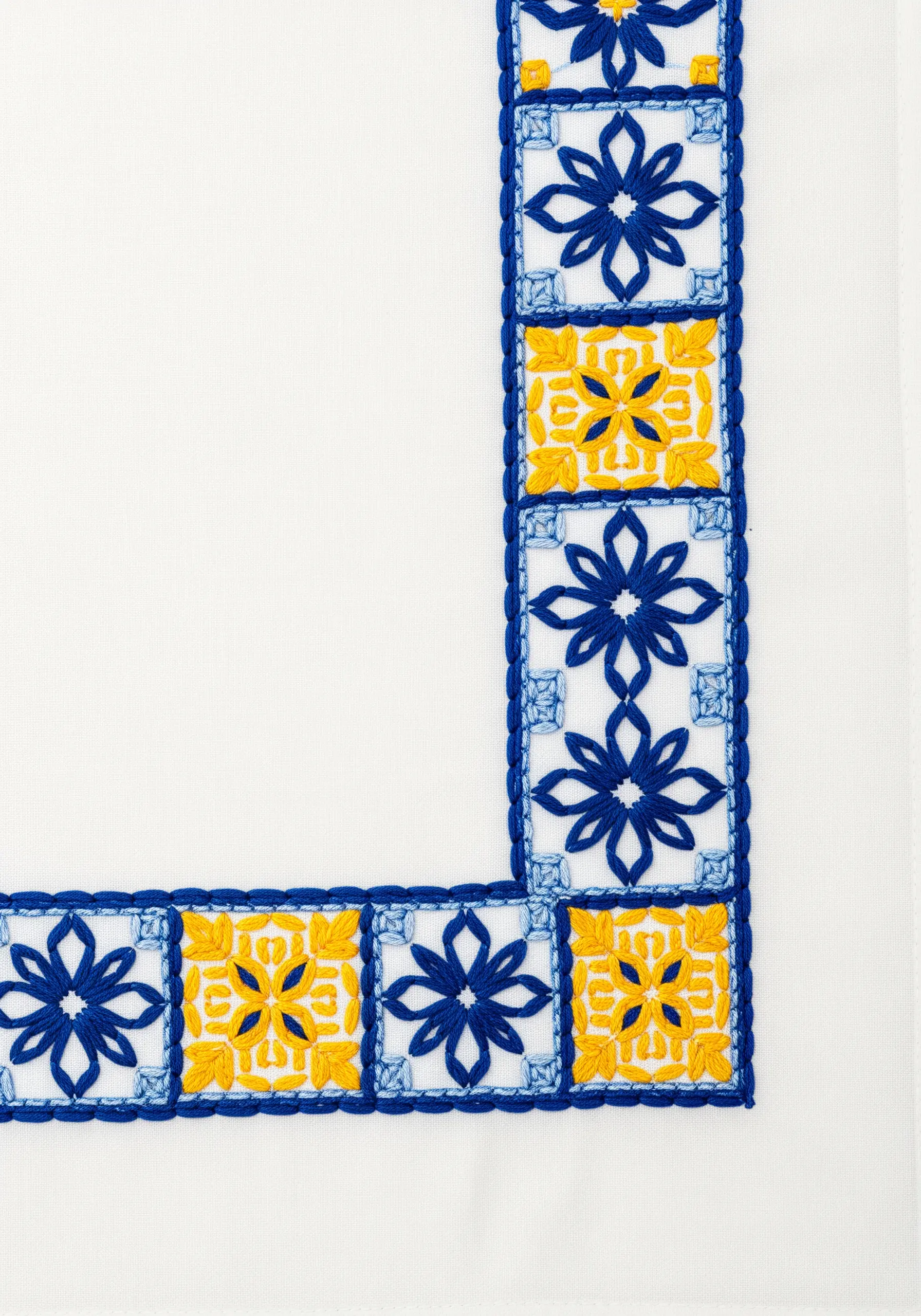 A crisp embroidered border of blue and yellow geometric tiles on a white napkin.