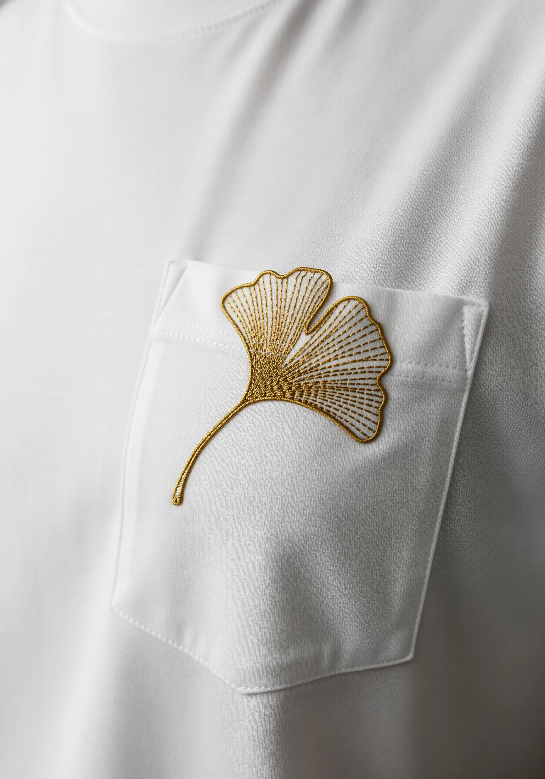 An elegant gold ginkgo leaf with detailed stitching on a t-shirt pocket.