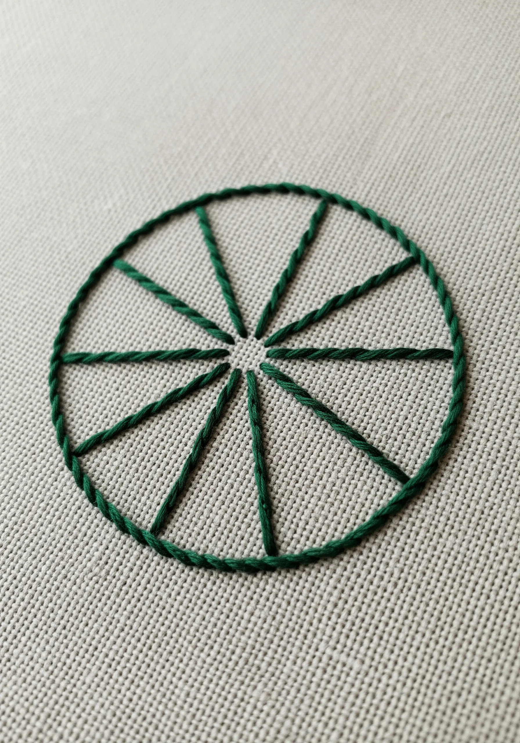 A simple green mandala with twelve spokes made from a raised rope stitch.