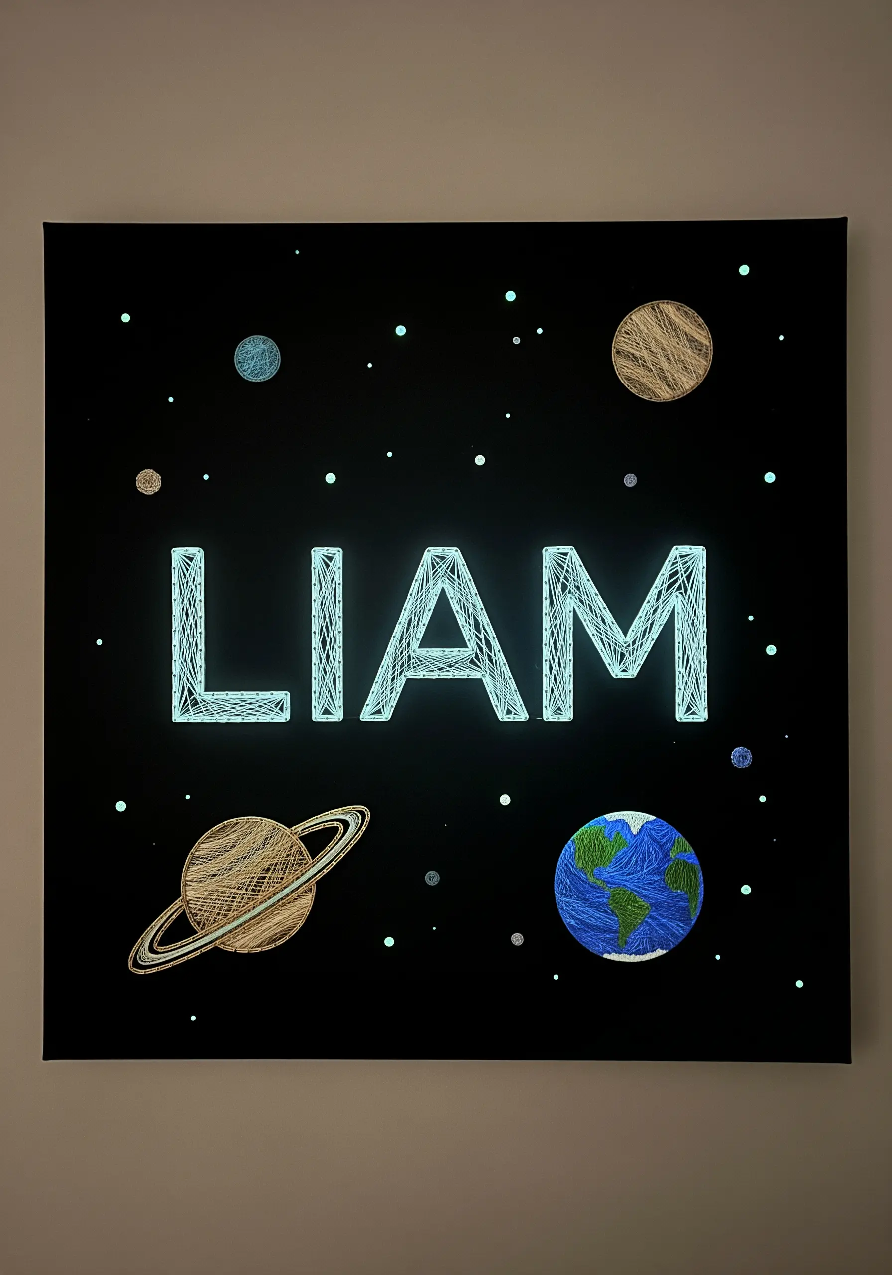 A name embroidered with glow-in-the-dark thread amidst stitched planets on black fabric.
