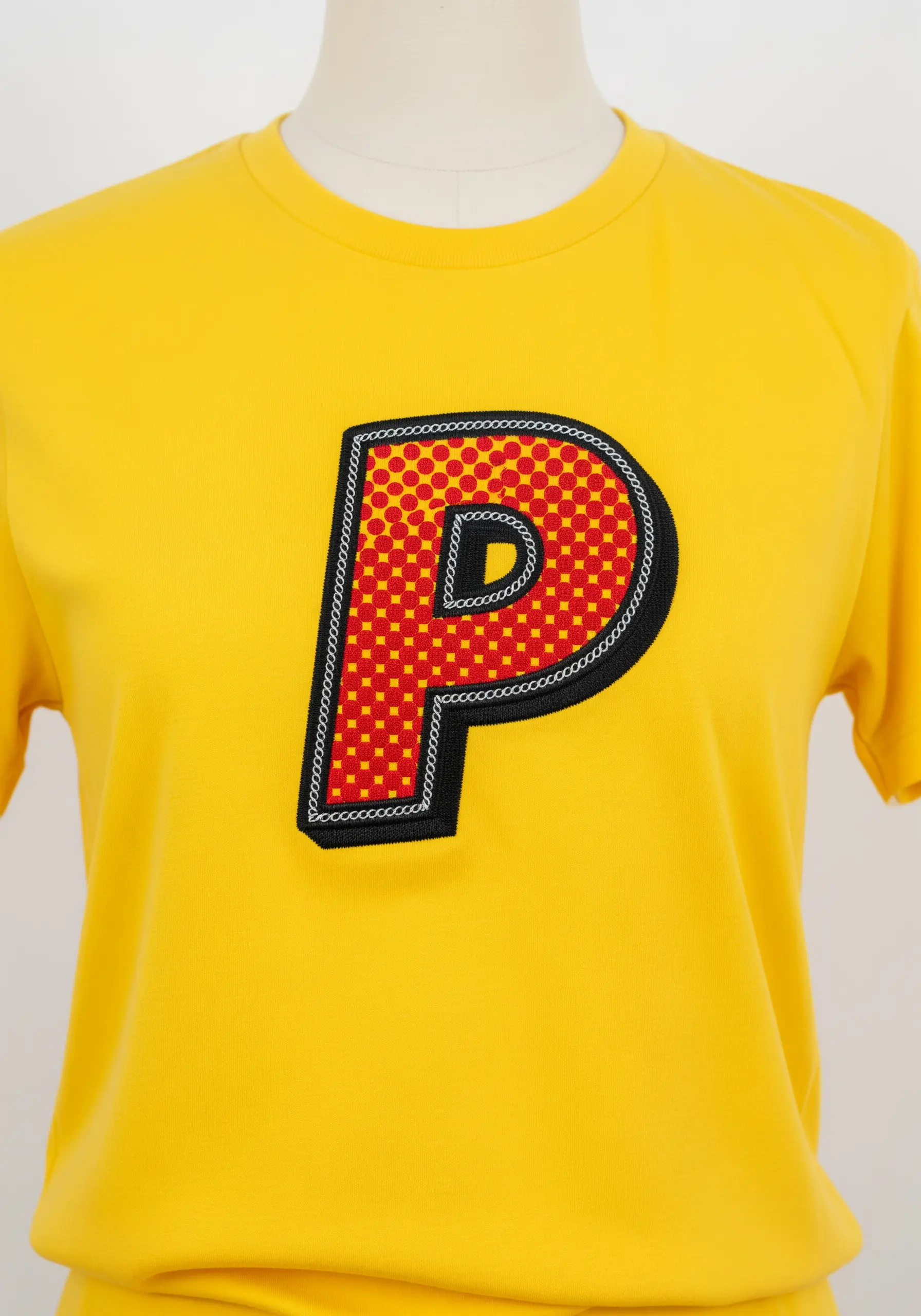 A pop-art style letter 'P' with a red polka-dot fill, black outline, and chain link detail.