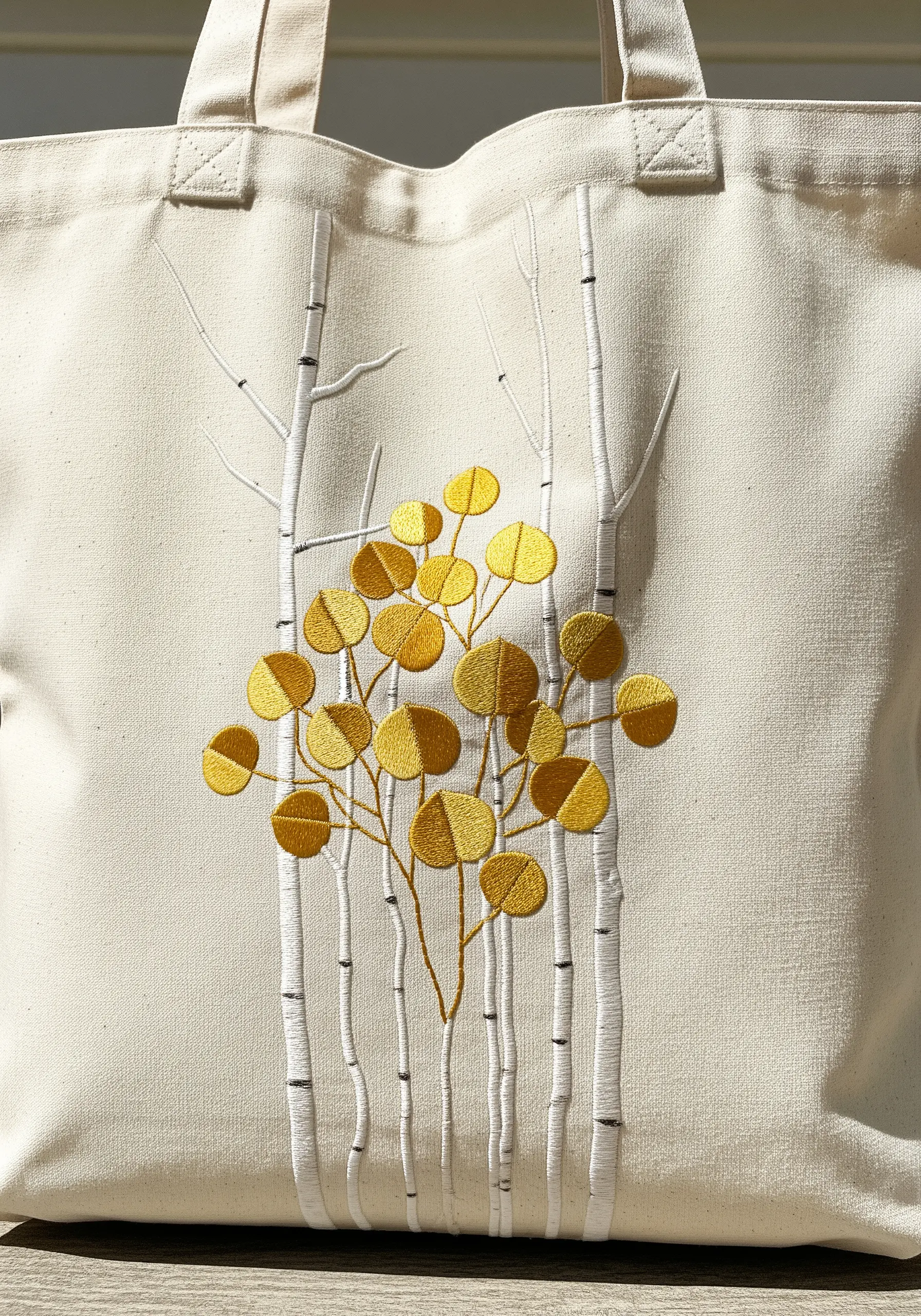 Embroidered golden aspen leaves in front of white stitched birch tree trunks.