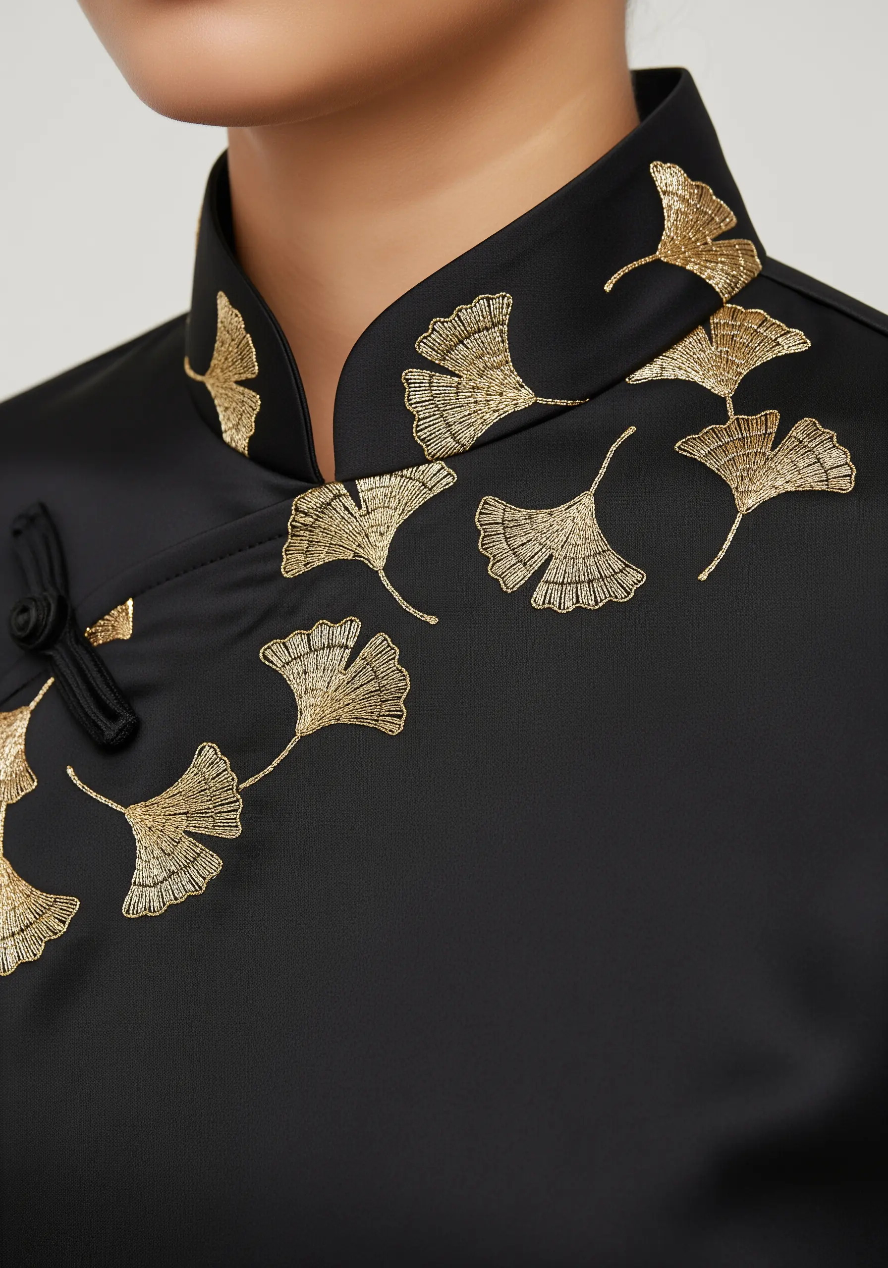 Golden metallic ginkgo leaves embroidered on the Mandarin collar of a black satin shirt.
