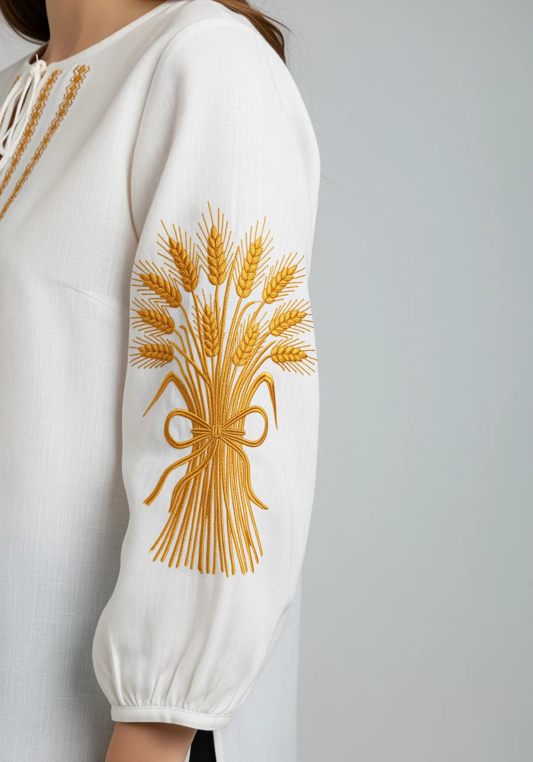 A golden sheaf of wheat embroidered in satin and stem stitch on the sleeve of a white linen blouse.
