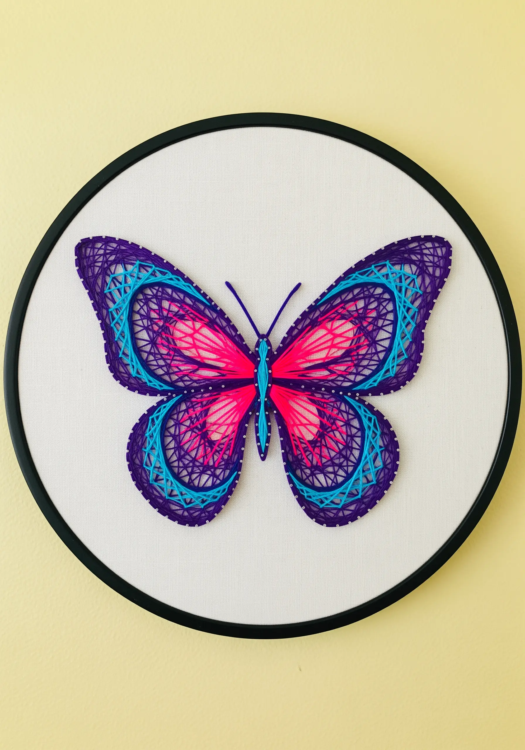 A vibrant butterfly embroidered with intricate, web-like patterns on its wings in pink, purple, and blue.