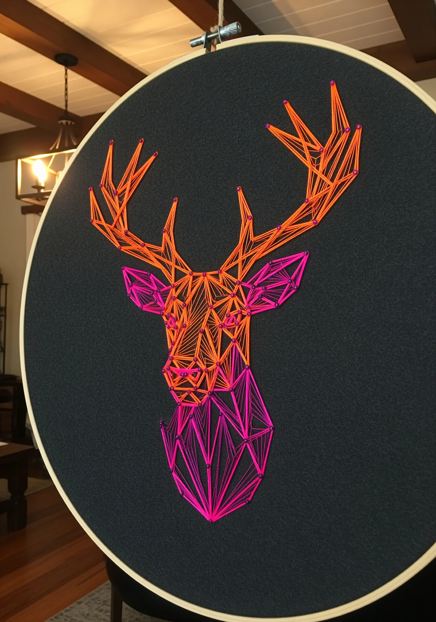 Geometric deer head embroidery with a neon orange-to-pink gradient on dark gray fabric.