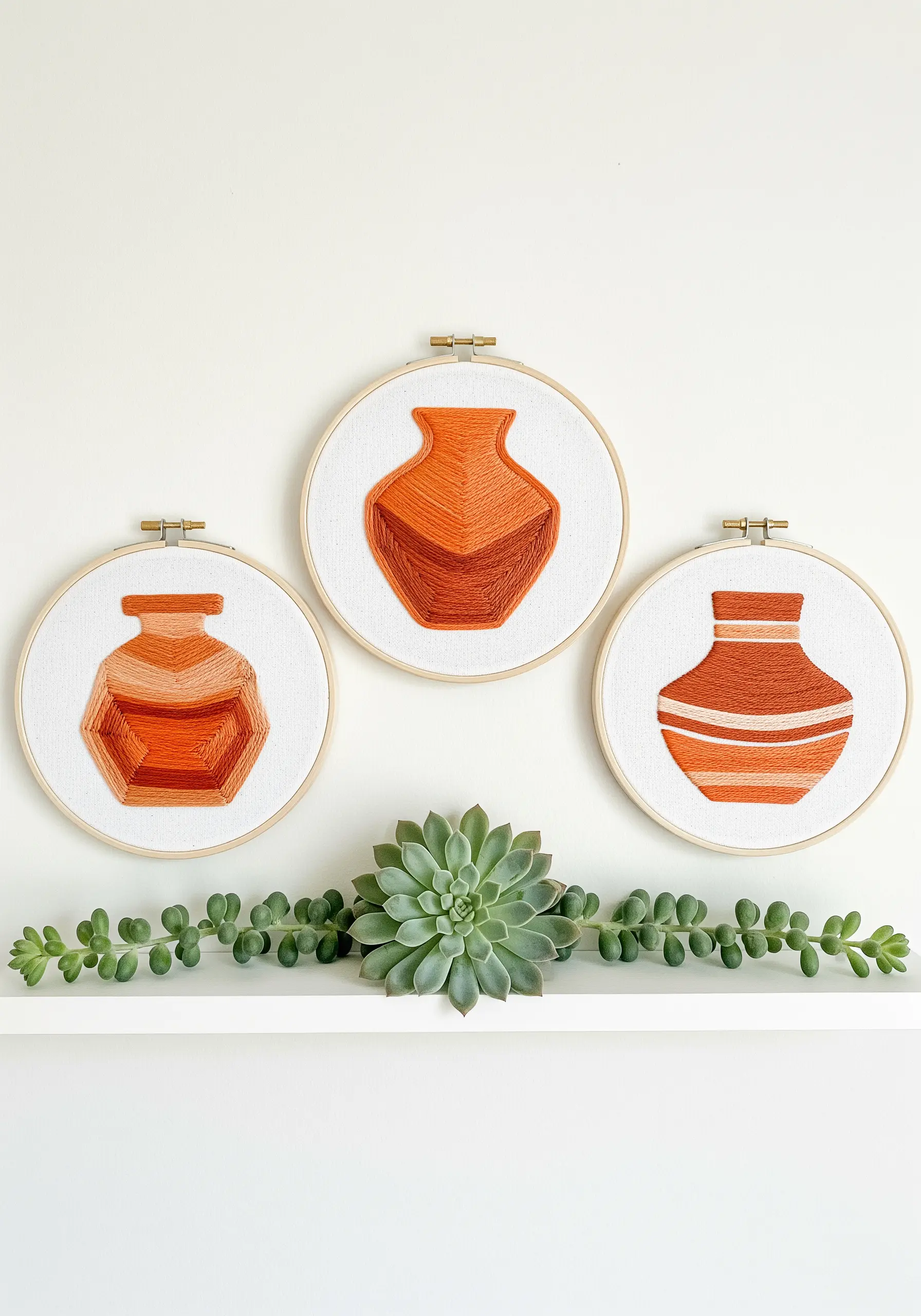 Triptych of embroidery hoops, each showing a terracotta-colored vase with graphic, color-blocked stripes.