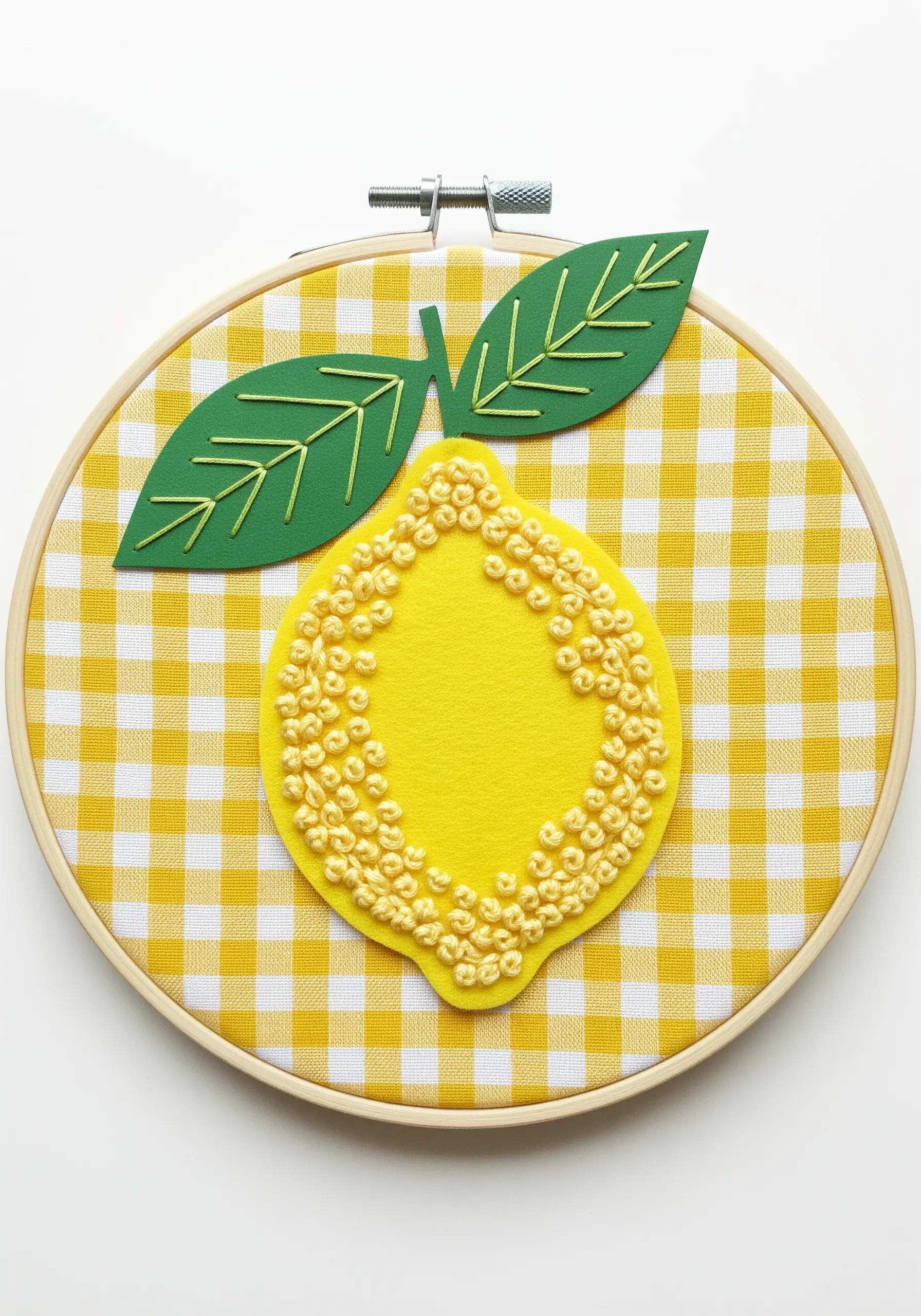 A lemon made from yellow felt on a gingham background, with the center filled with French knots.