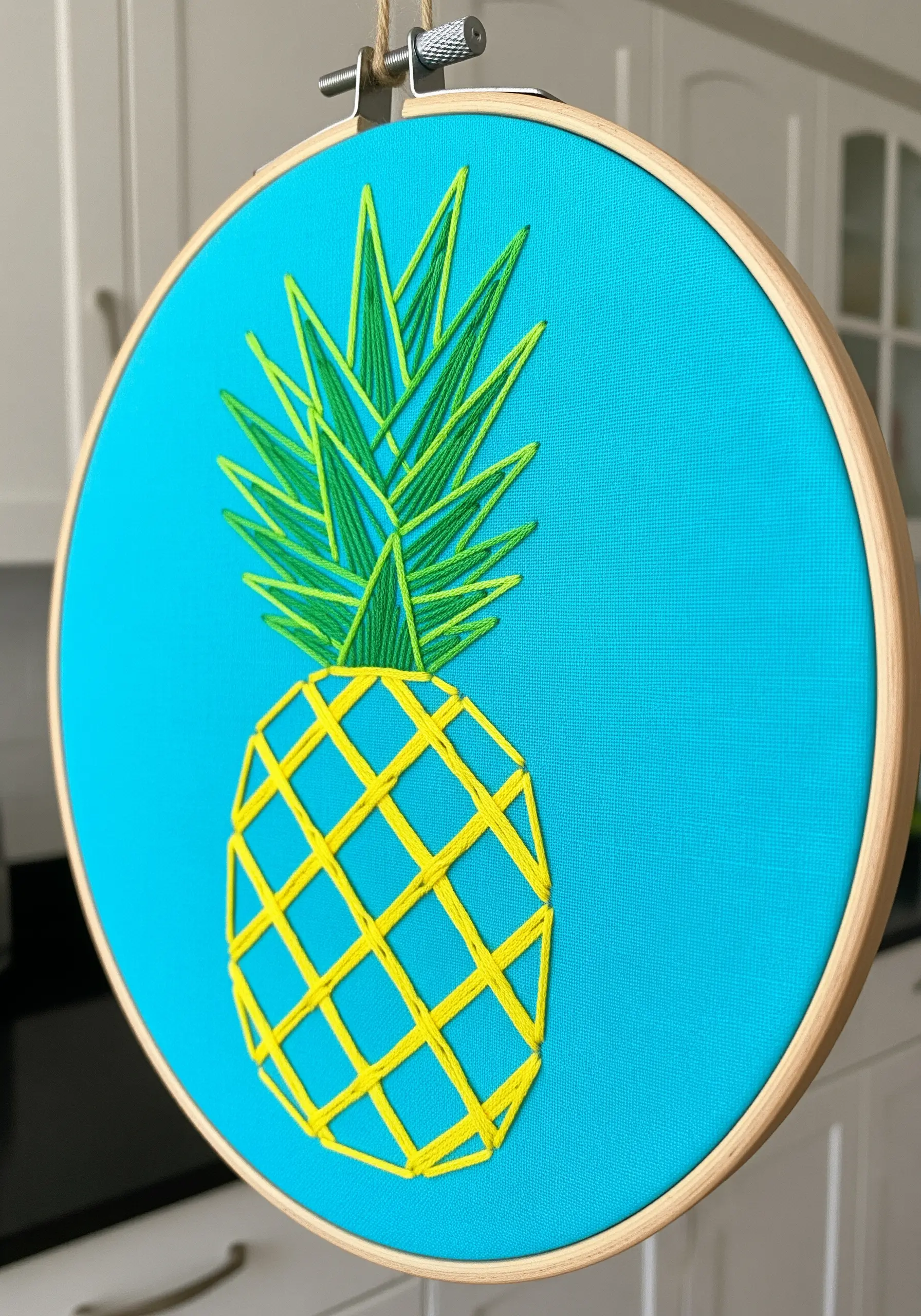 A minimalist string art pineapple with yellow and green thread on a bright blue background.