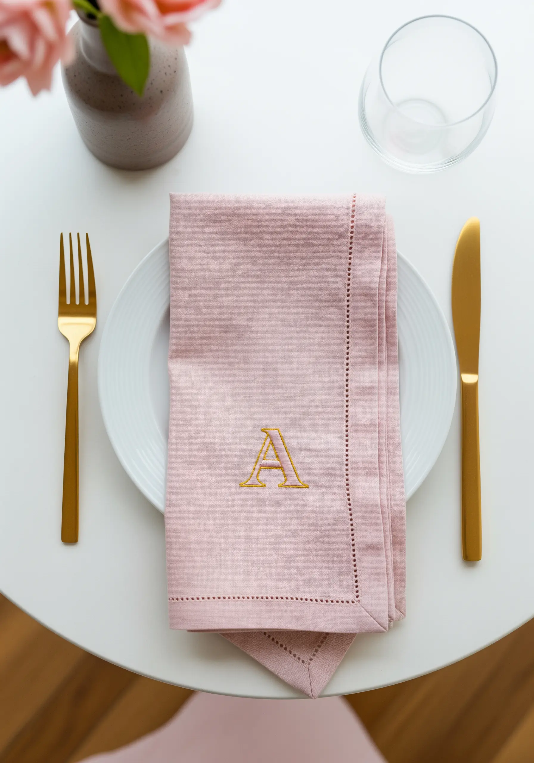 Pink linen napkin on a white plate with a gold embroidered letter 'A' monogram