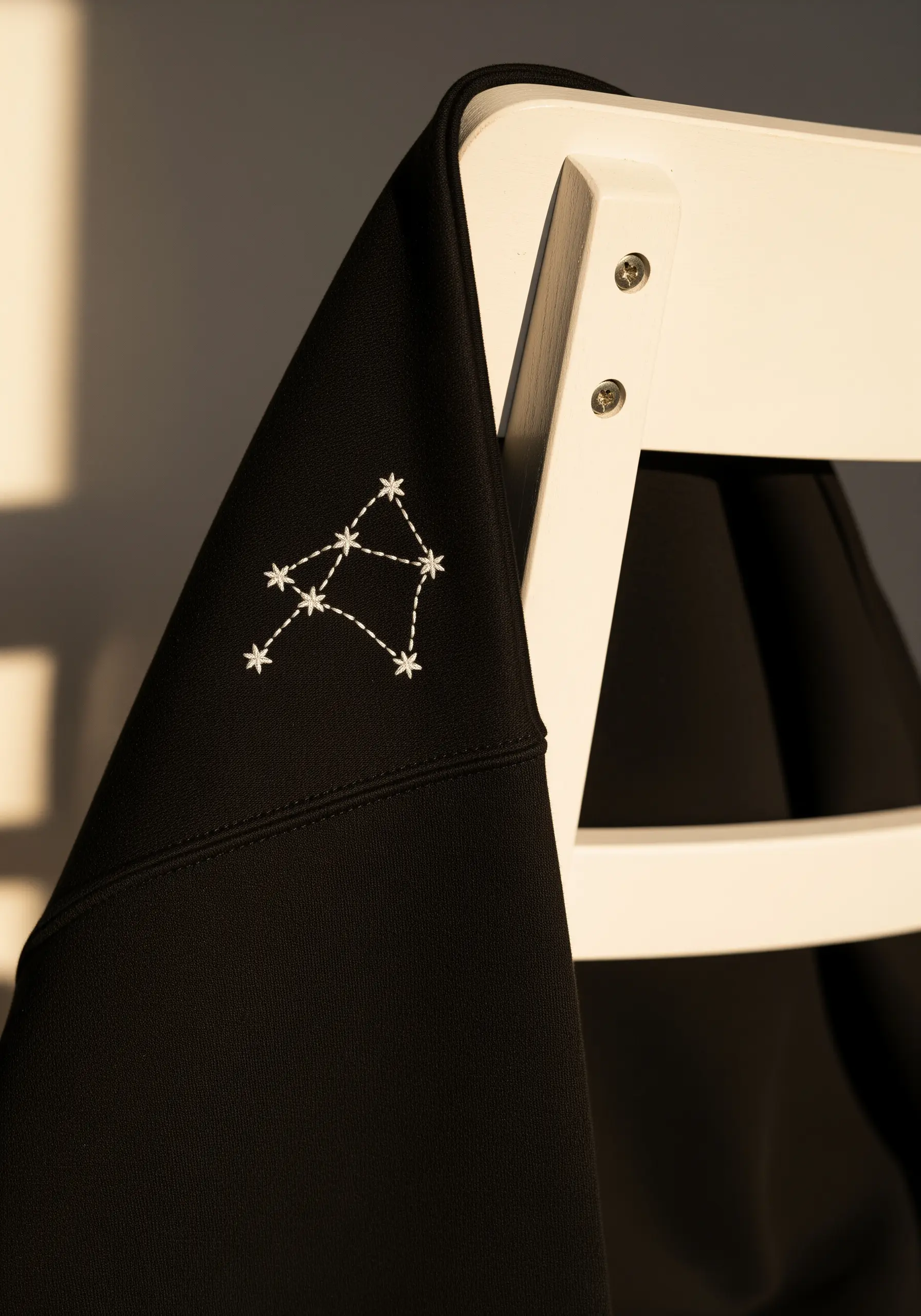 A minimalist white thread constellation stitched on the shoulder of a black hoodie.