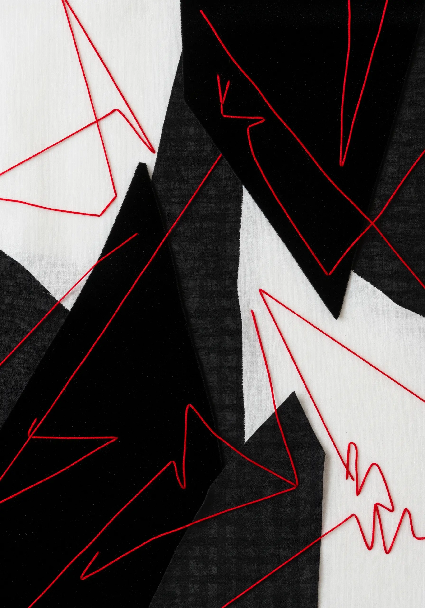 A stark black and white fabric collage with a vibrant red thread creating sharp, angular lines.
