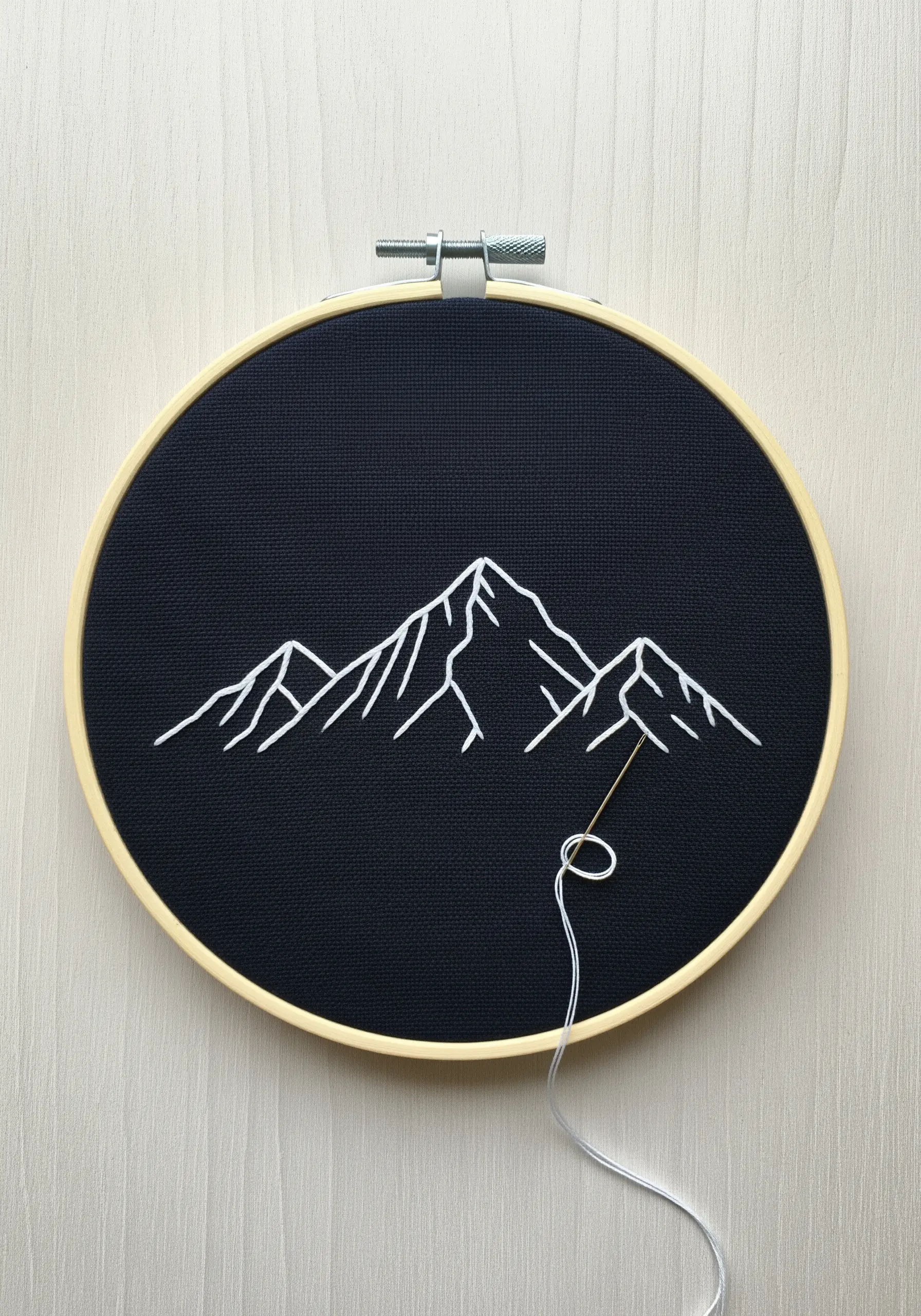Minimalist white line art of a mountain range embroidered on black fabric.