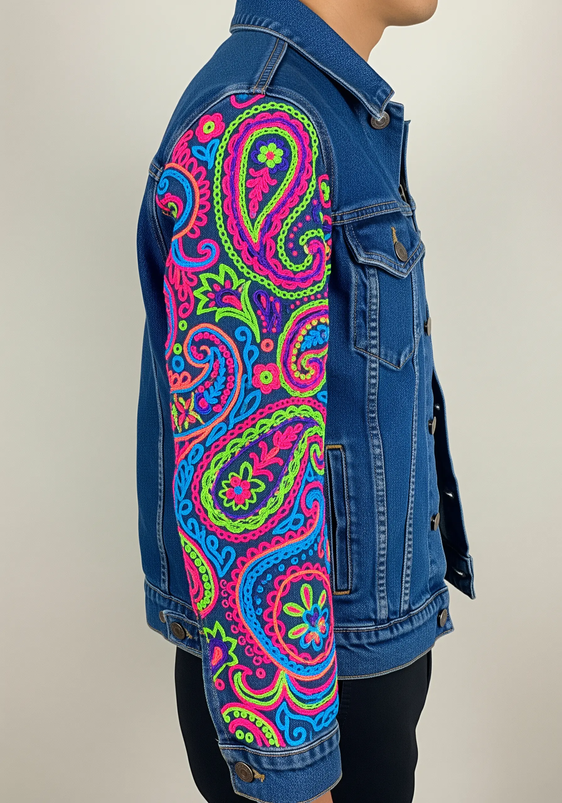 A full sleeve of bold, neon paisley patterns embroidered in pink, green, and blue on a denim jacket.