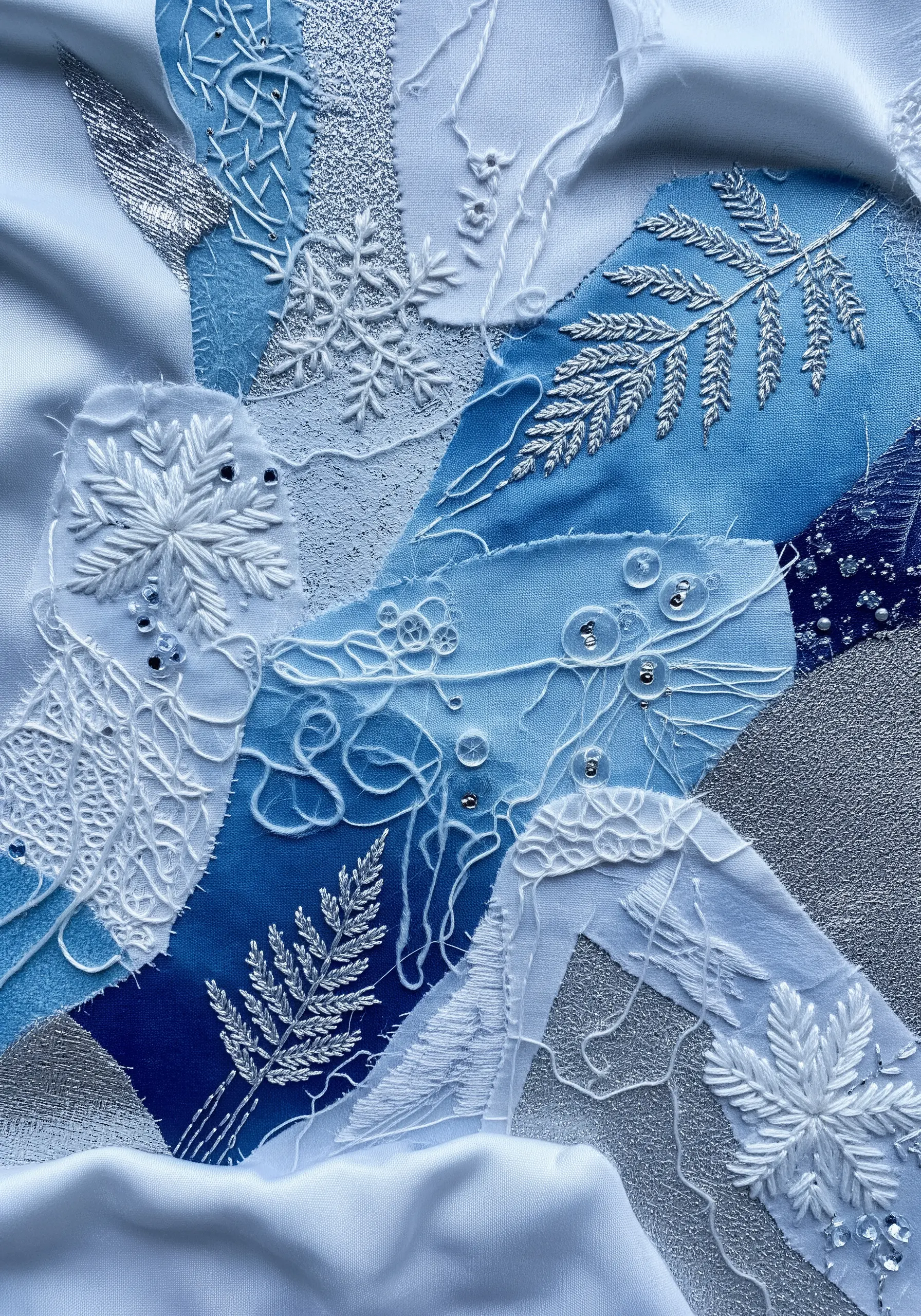 A winter-themed collage of blue and white fabrics with silver embroidery and clear bead accents.