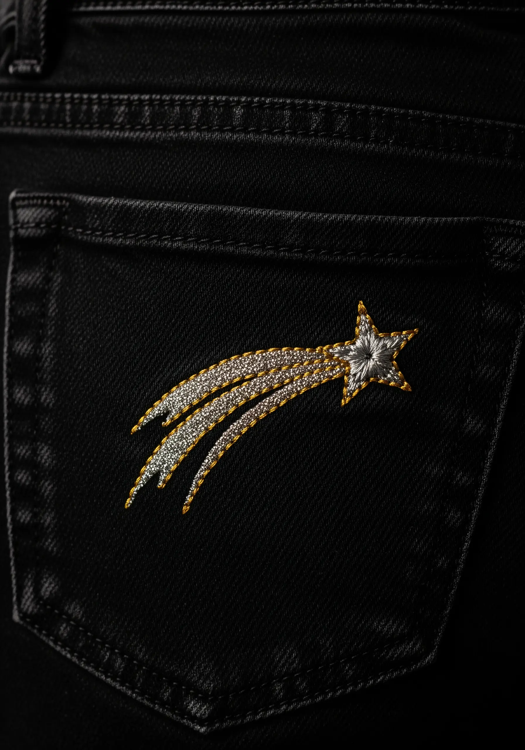 A shooting star embroidered with gold and silver metallic thread on a black denim pocket.