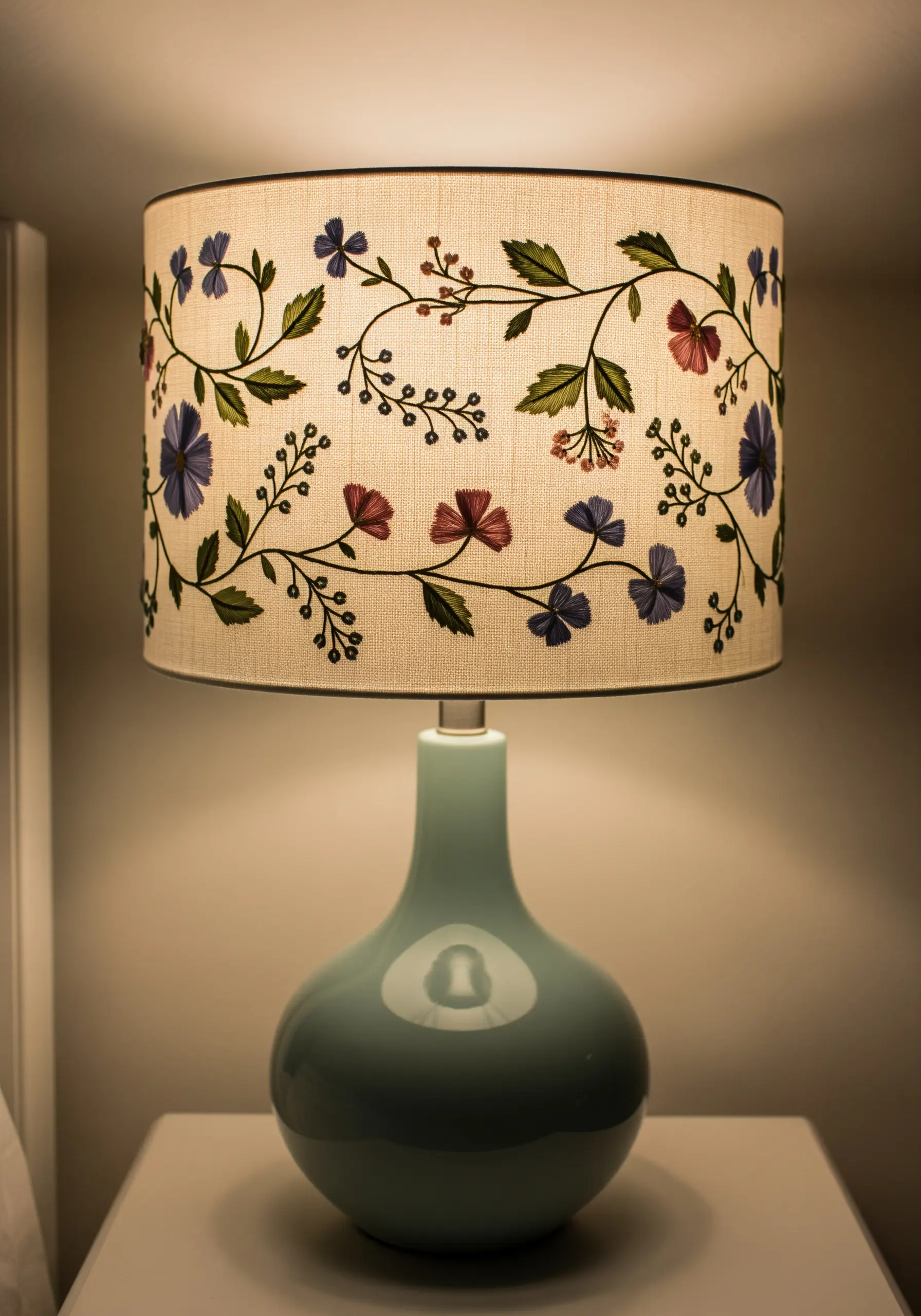 A fabric lampshade decorated with a winding floral and botanical embroidery pattern.