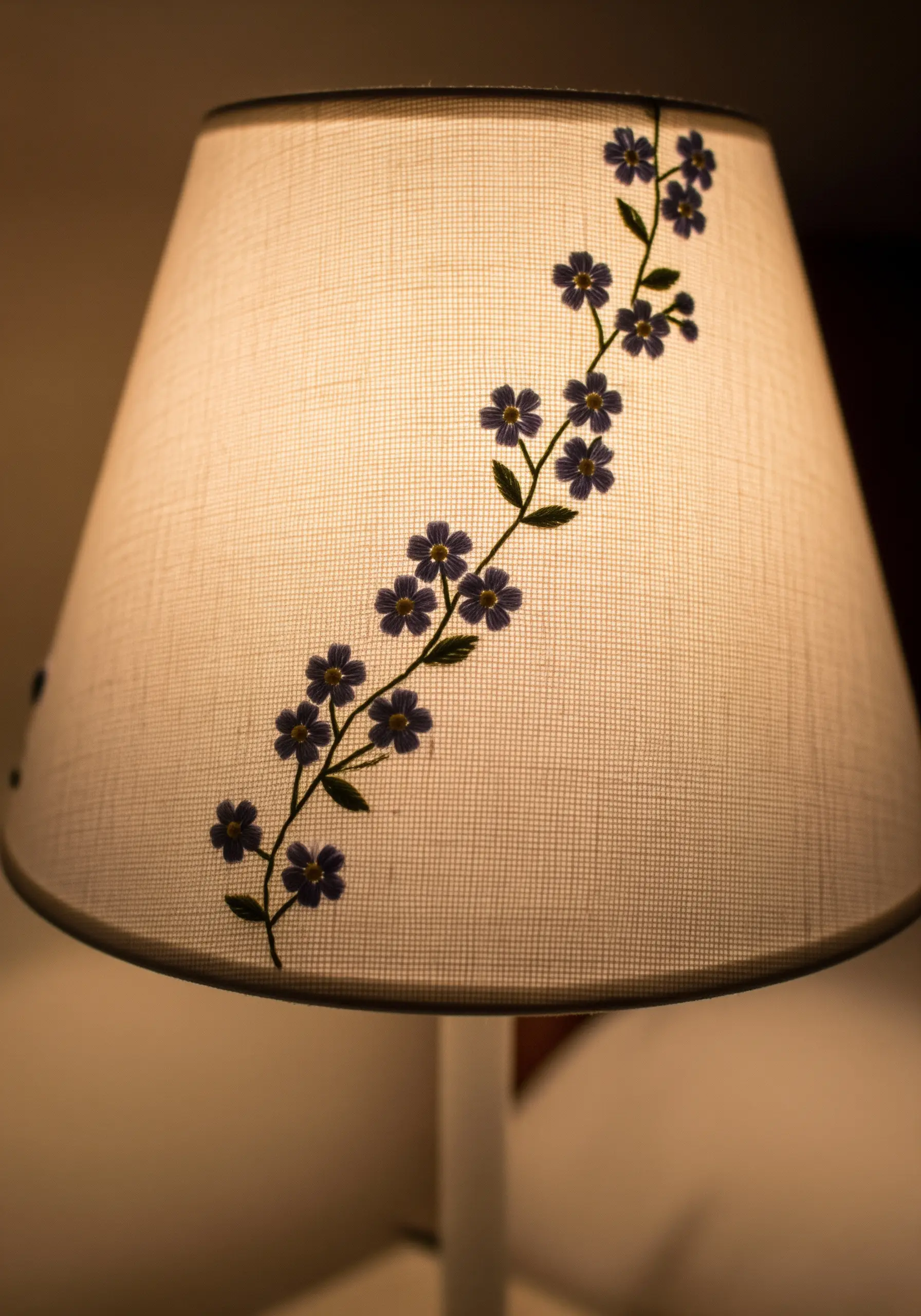 A simple vine of purple flowers embroidered vertically on a cream-colored fabric lampshade.