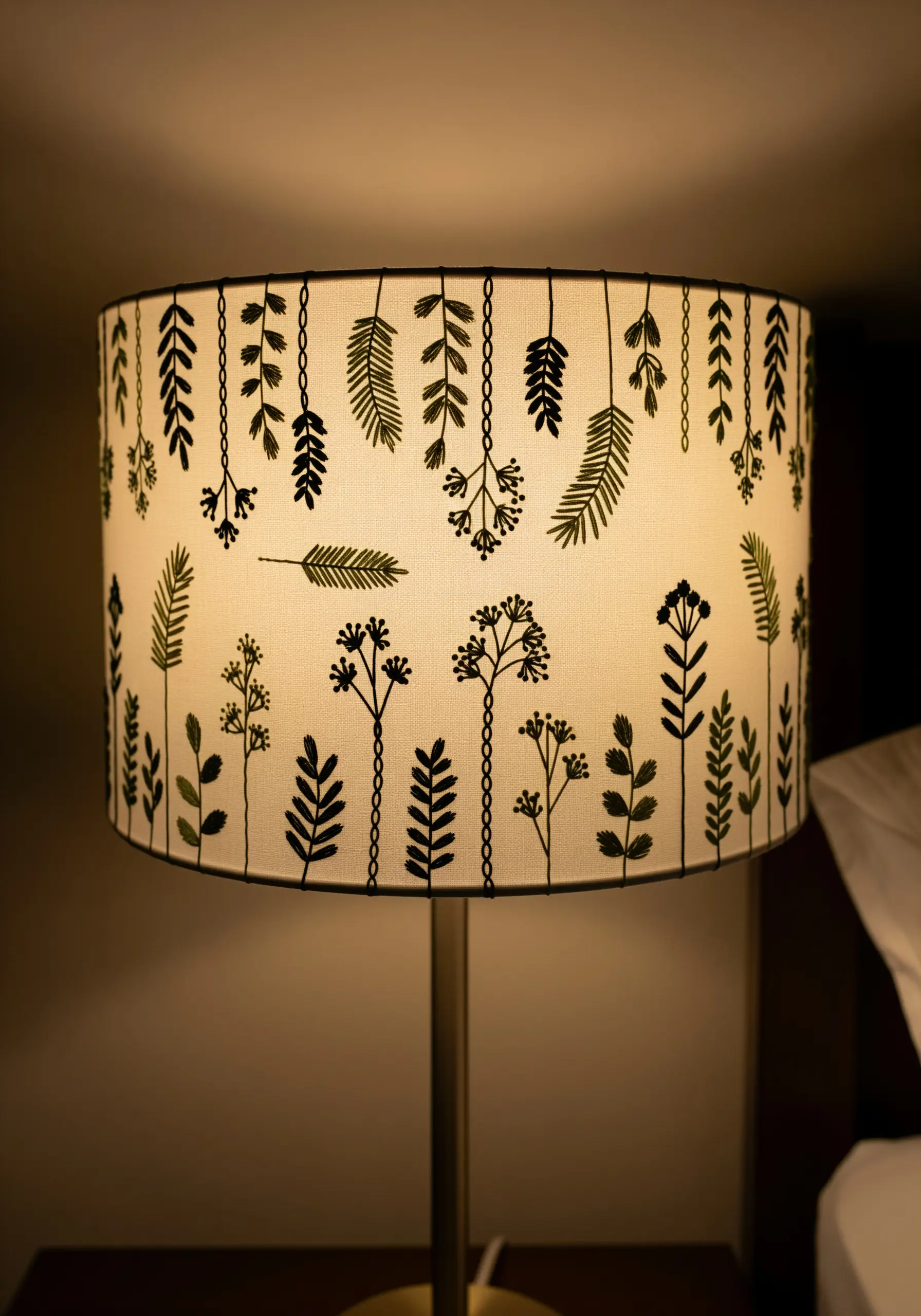 A linen lampshade with embroidered black botanical and leaf silhouettes.