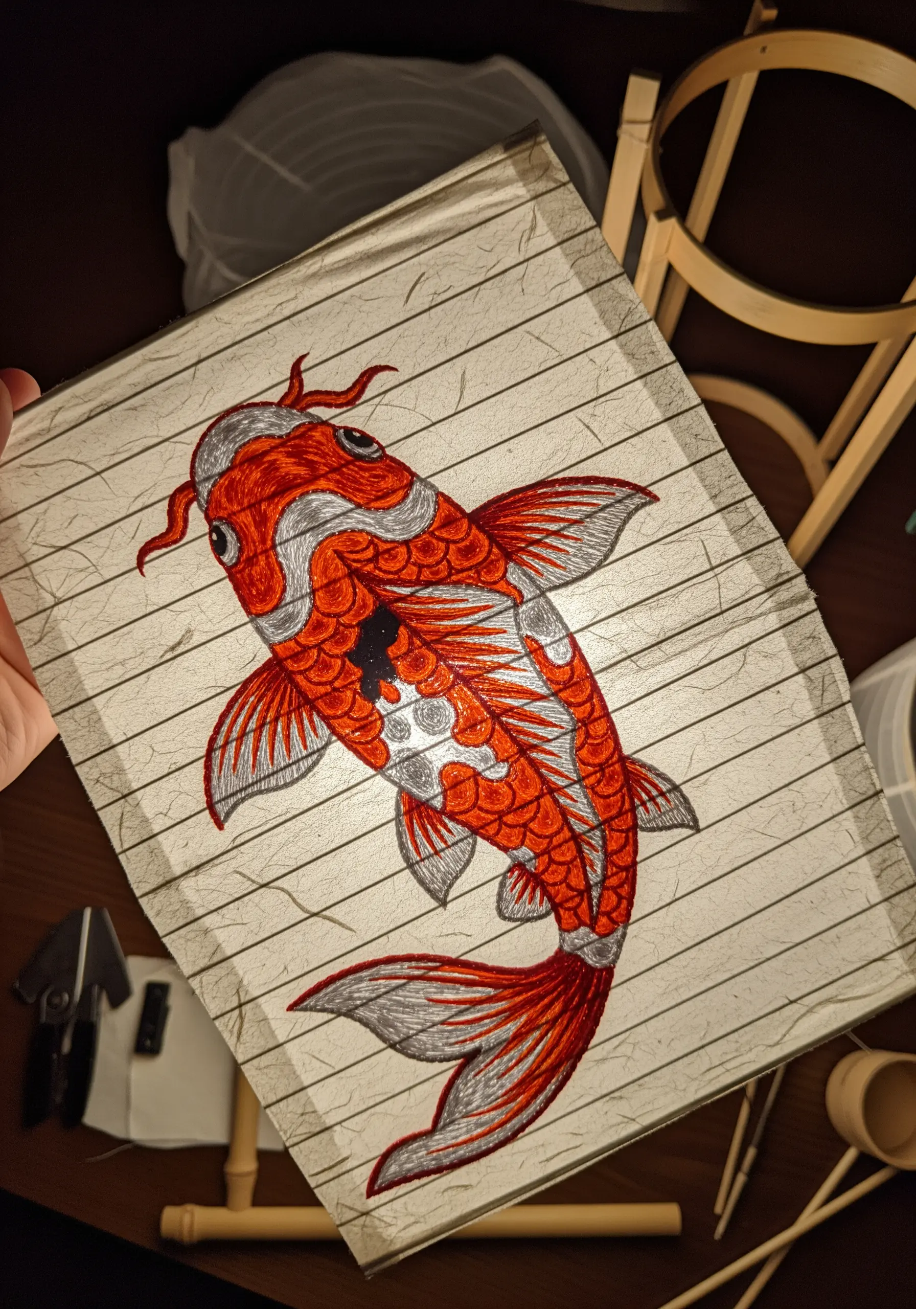 An embroidered red and silver koi fish on translucent paper, backlit like a lantern.