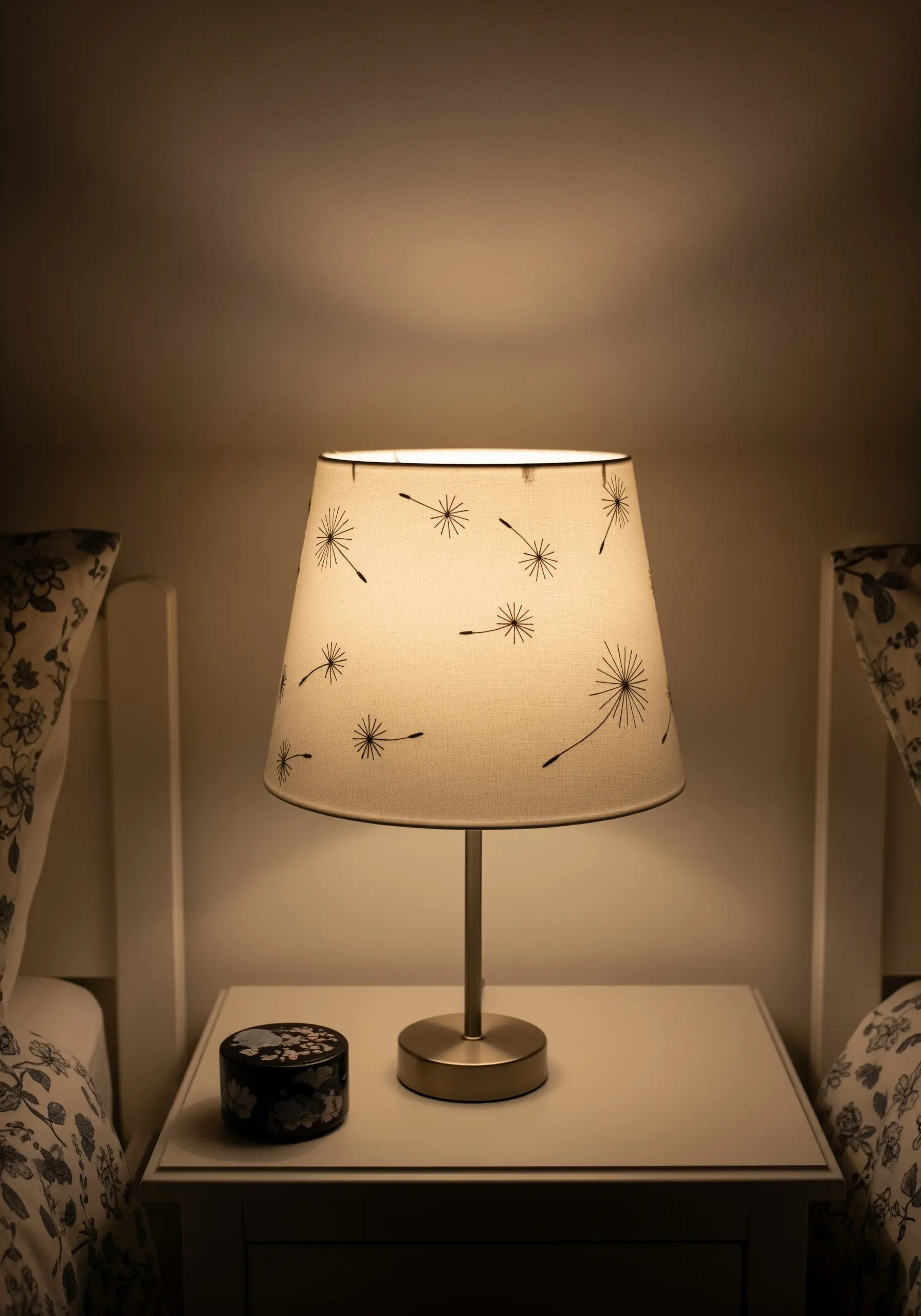 Dandelion seed motifs embroidered in dark thread scattered across a fabric lampshade.