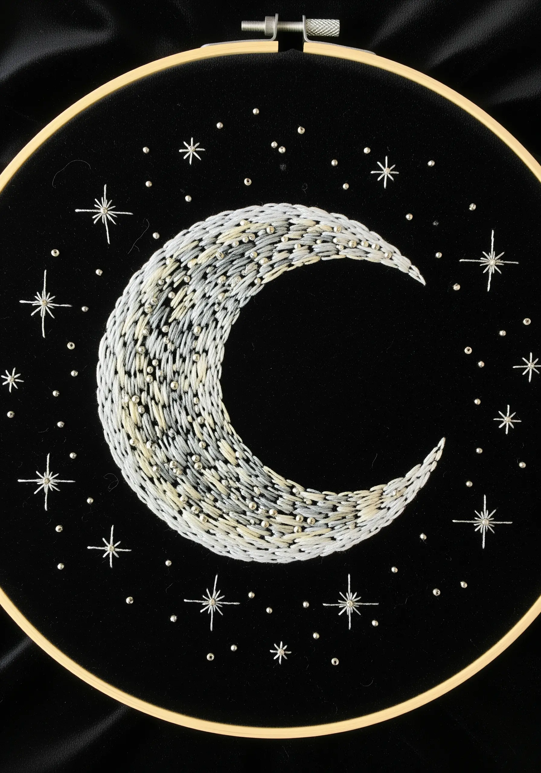 Embroidery of a crescent moon on black velvet, filled with white and silver threads and bugle beads.