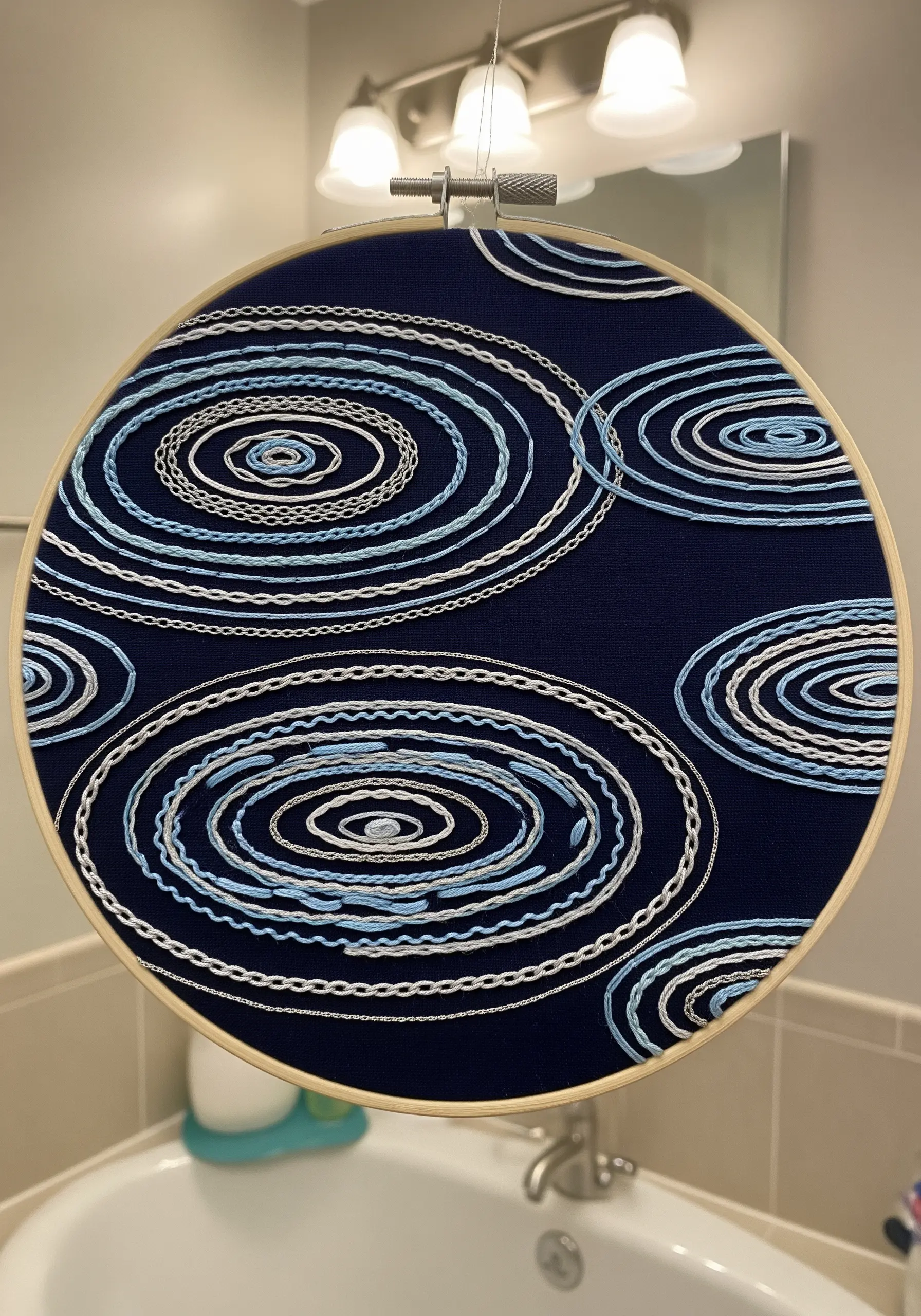 Embroidery hoop with concentric ovals in blue and white stitches, creating a water ripple effect.