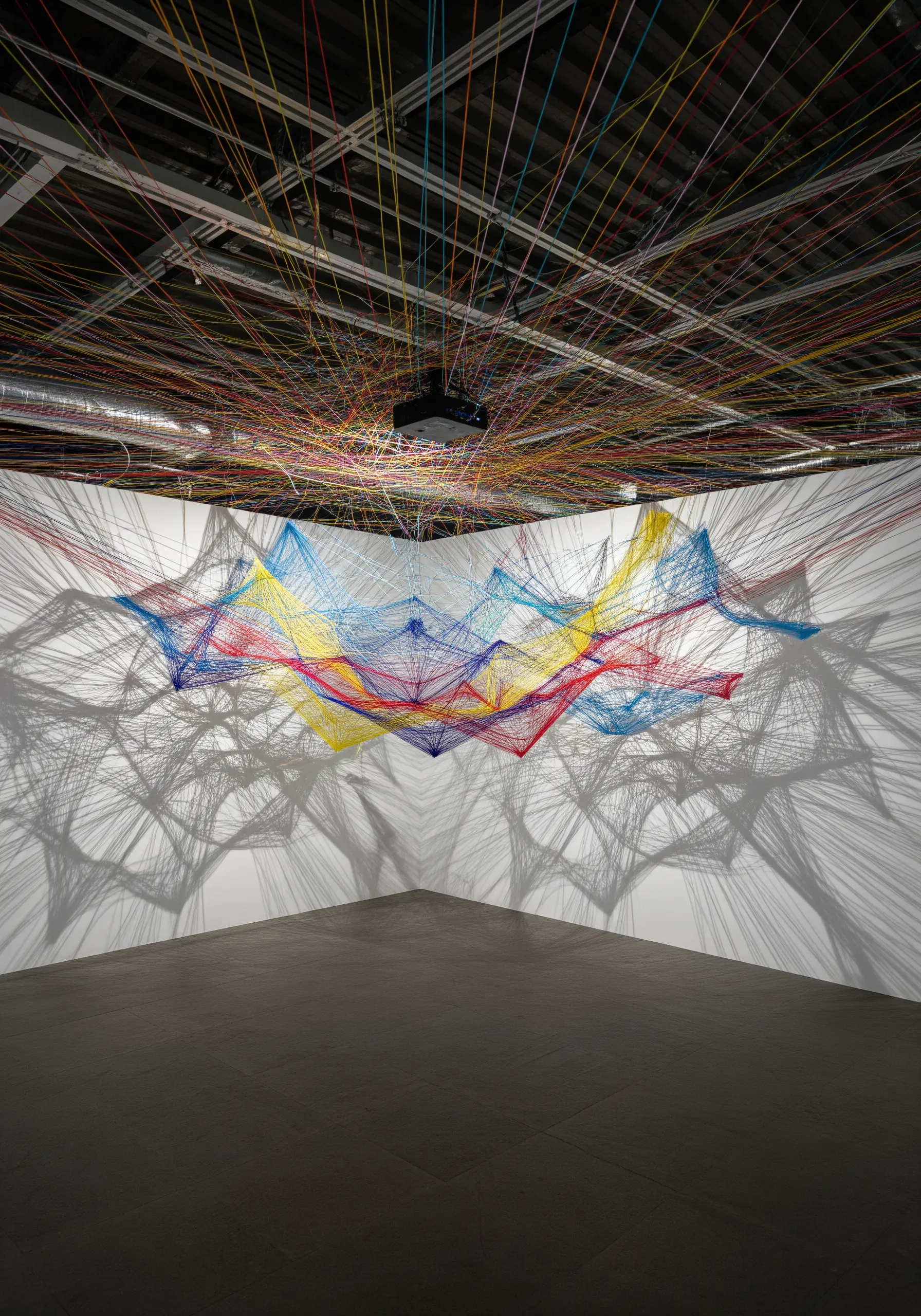 A room-scale installation with multicolored threads stretched from ceiling to walls.