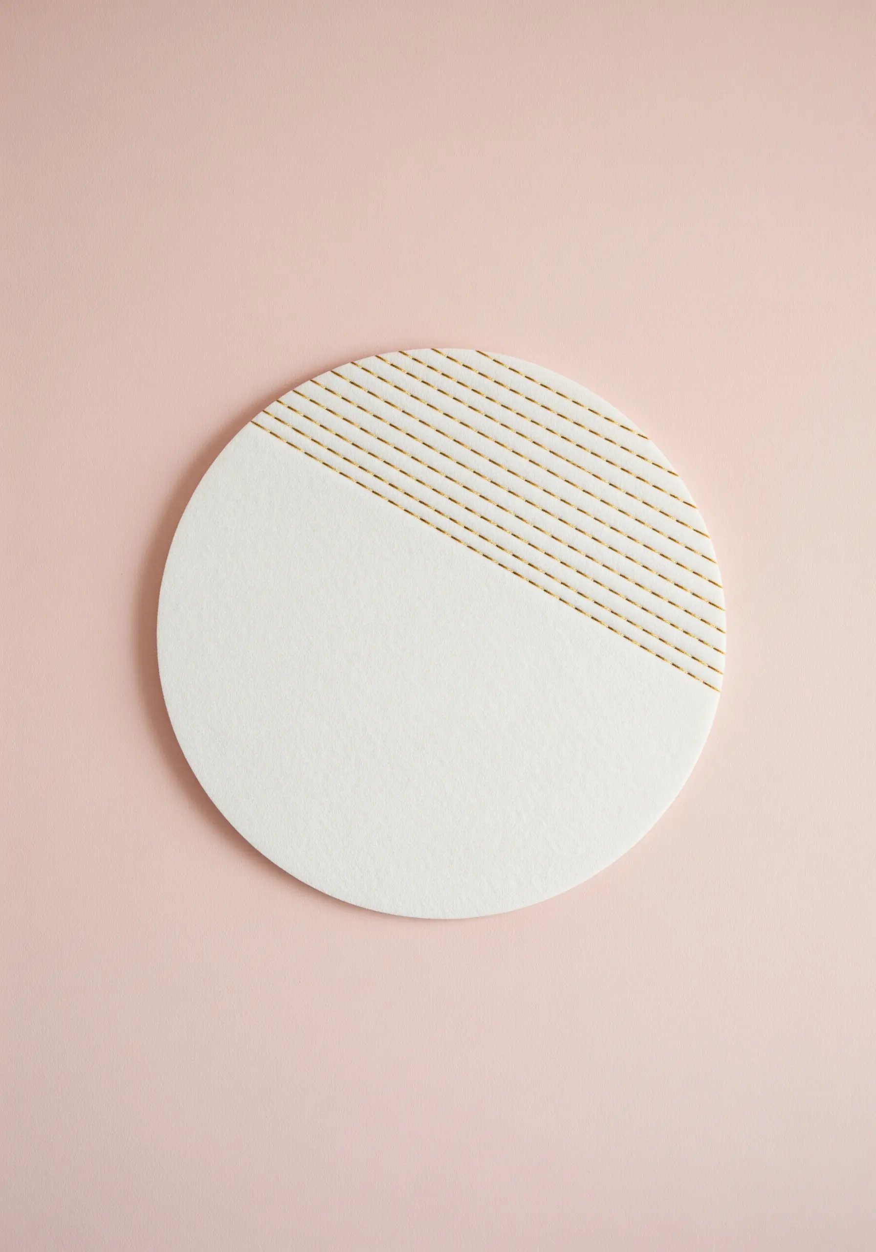 A close-up of parallel gold running stitches on a round, white disc against a pink background.