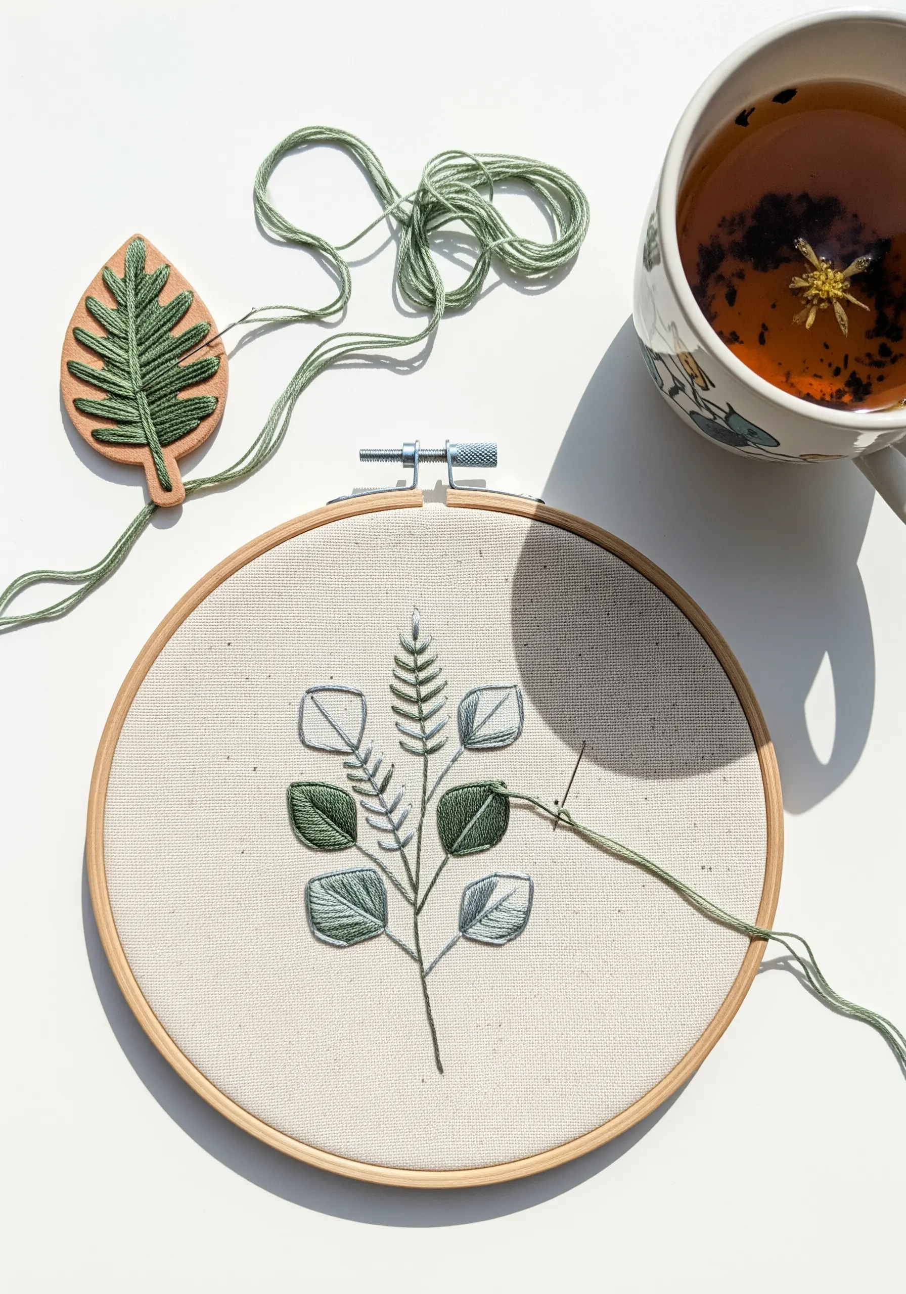 Minimalist embroidered botanical branch with varied satin stitch directions on leaves.