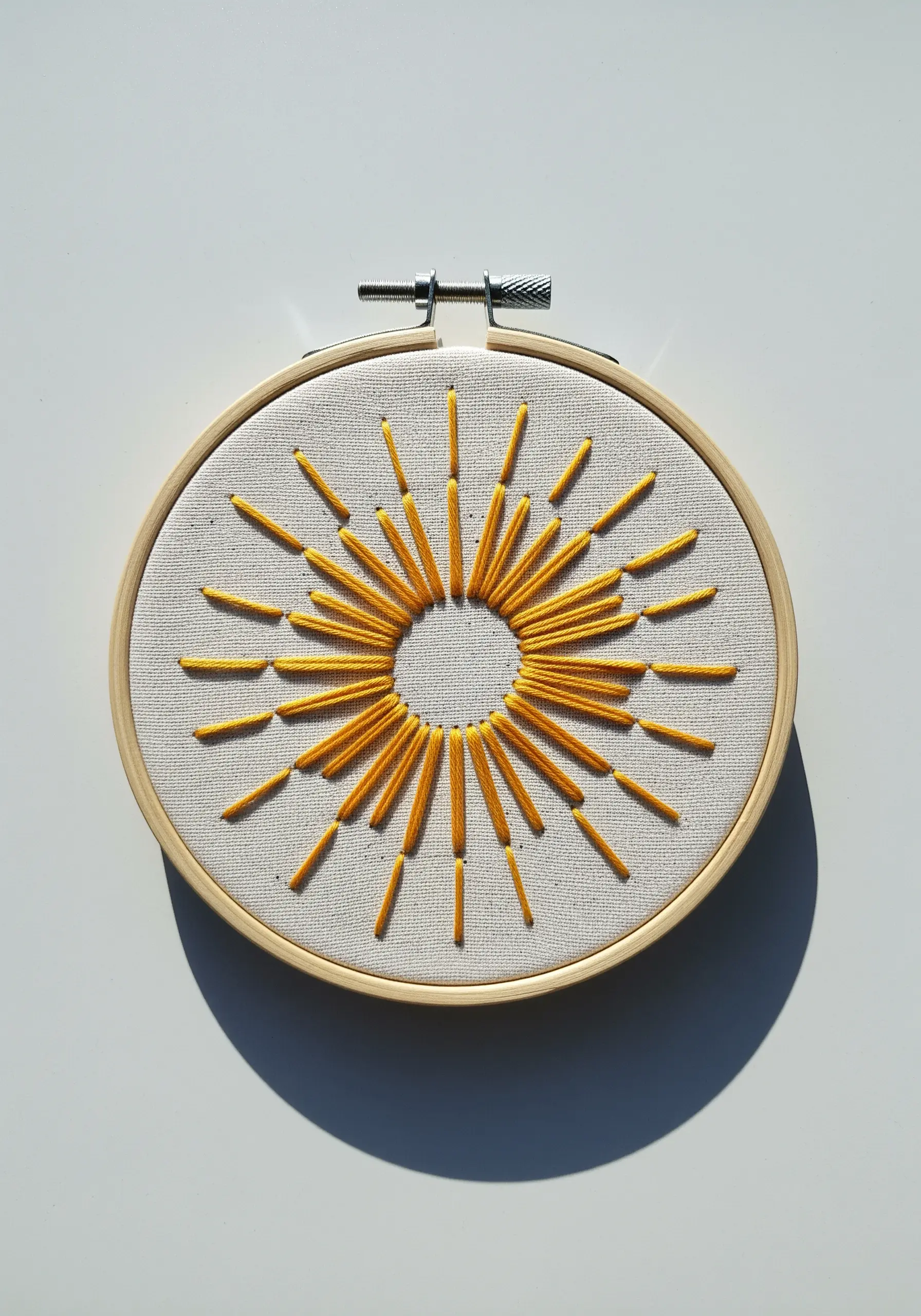 An abstract sunburst motif with radiating yellow straight stitches on a neutral fabric.