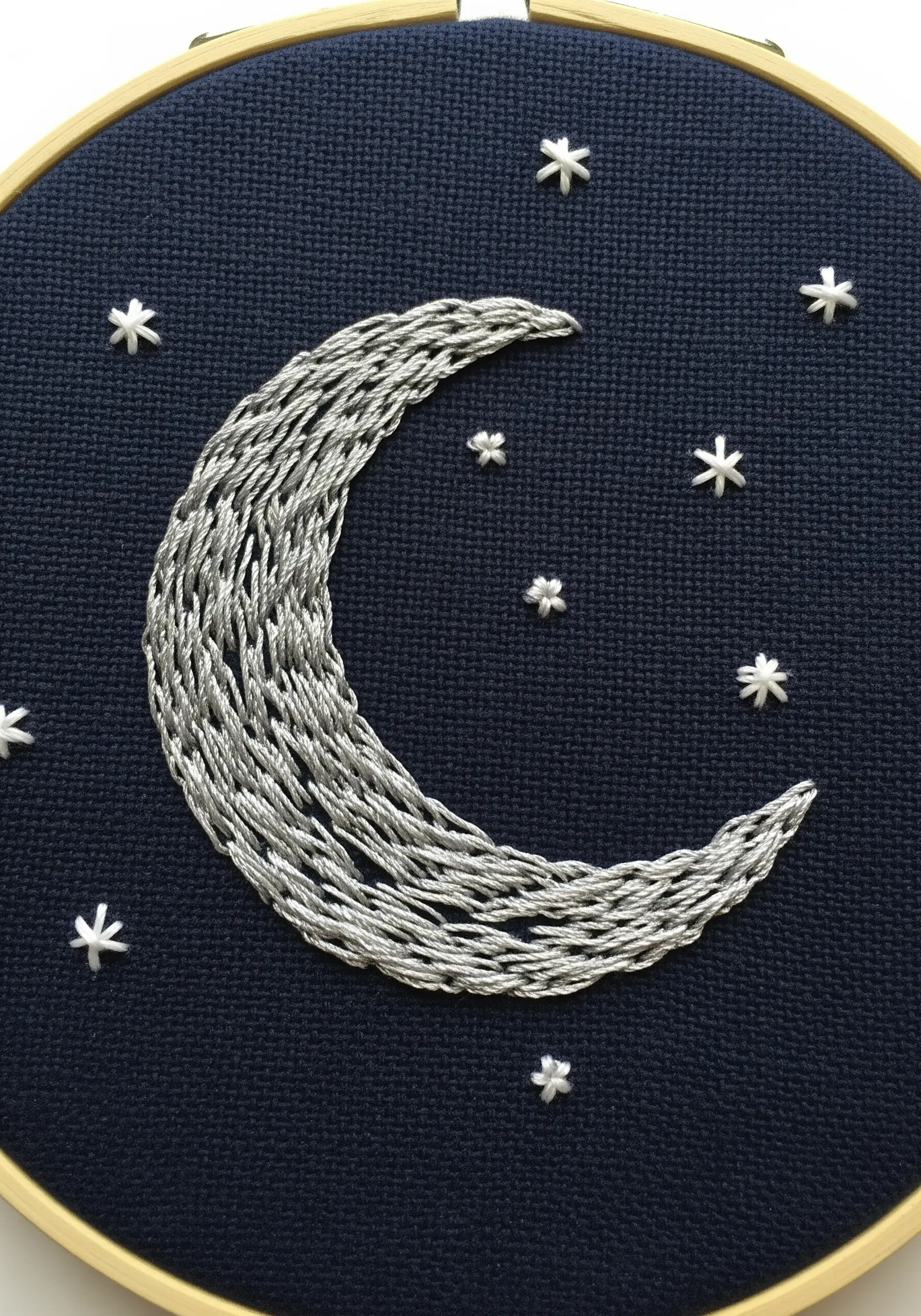 A crescent moon filled with textured silver thread on dark navy fabric with small star stitches.