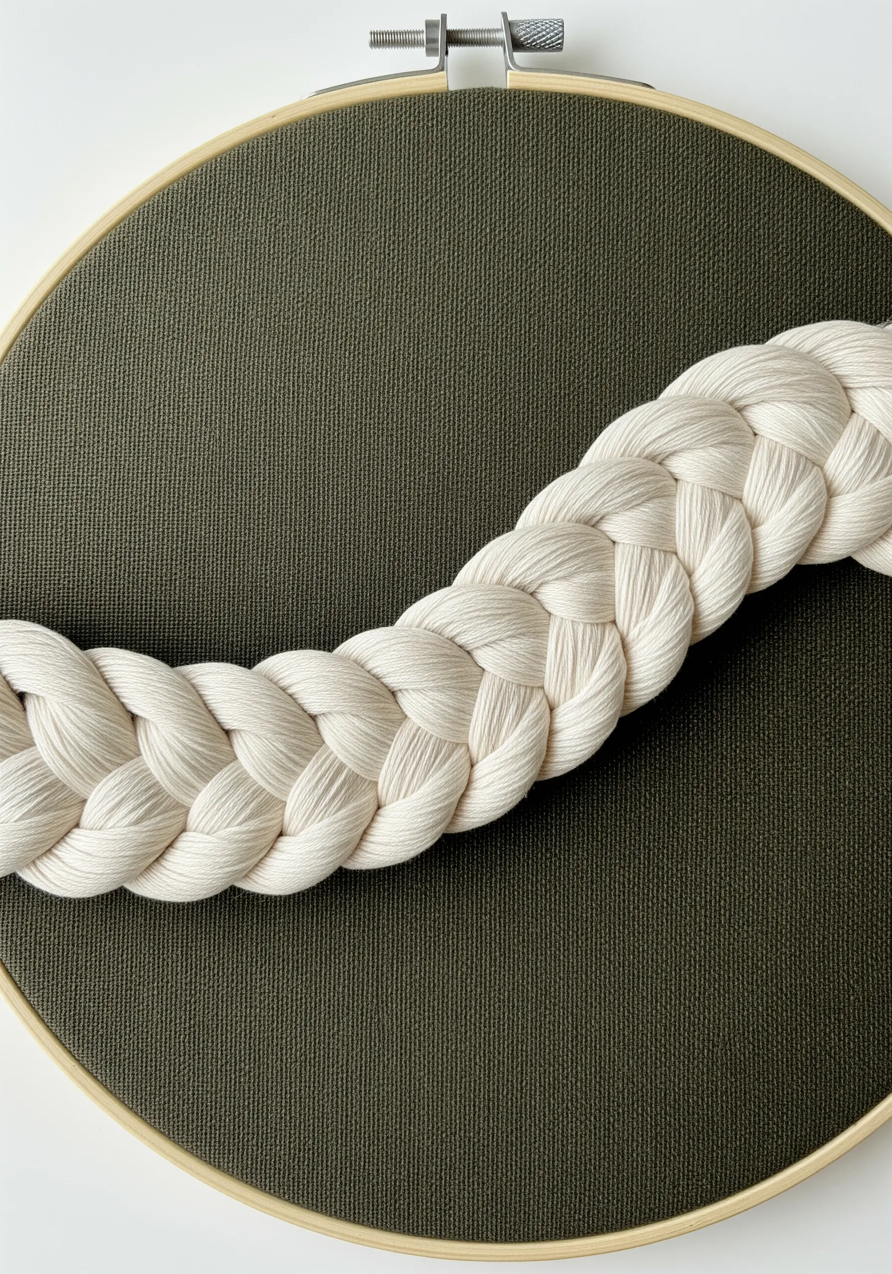 A thick, cream-colored macrame braid couched diagonally across a hoop.