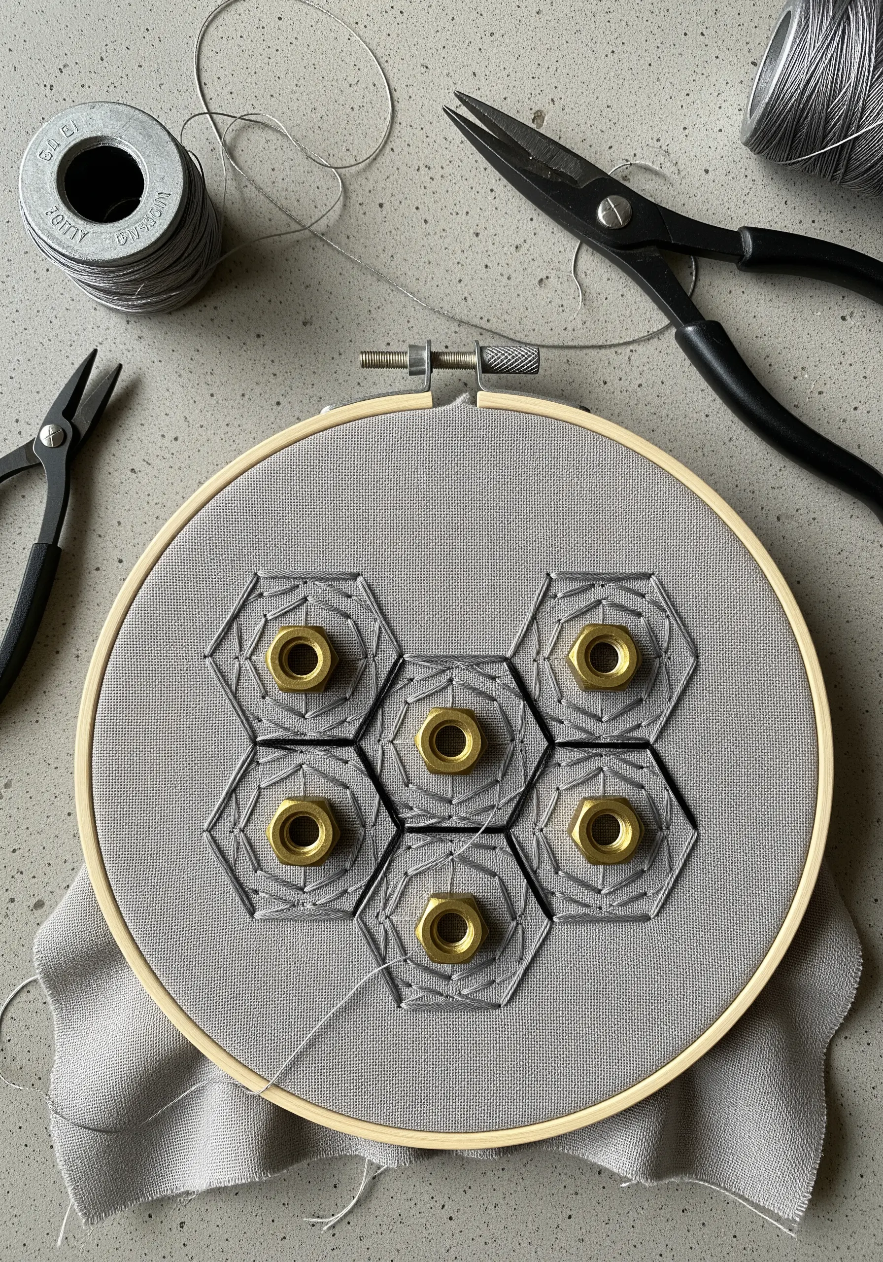 Geometric embroidery incorporating brass hex nuts on grey fabric