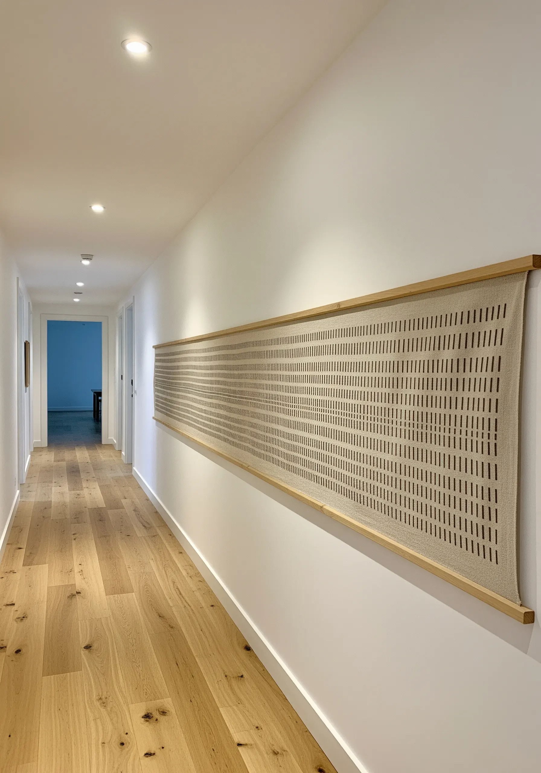 A long, narrow textile hanging in a hallway with minimalist vertical cutwork.