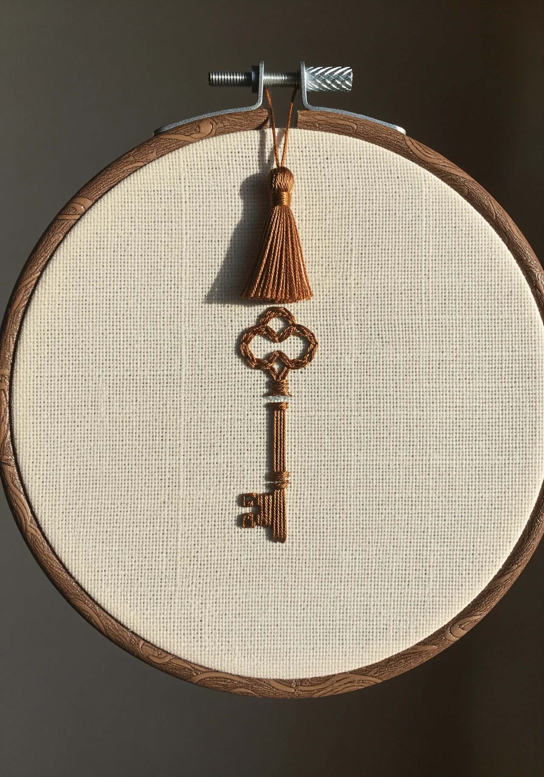 An embroidered vintage key in a hoop with a matching thread tassel hanging from the top.