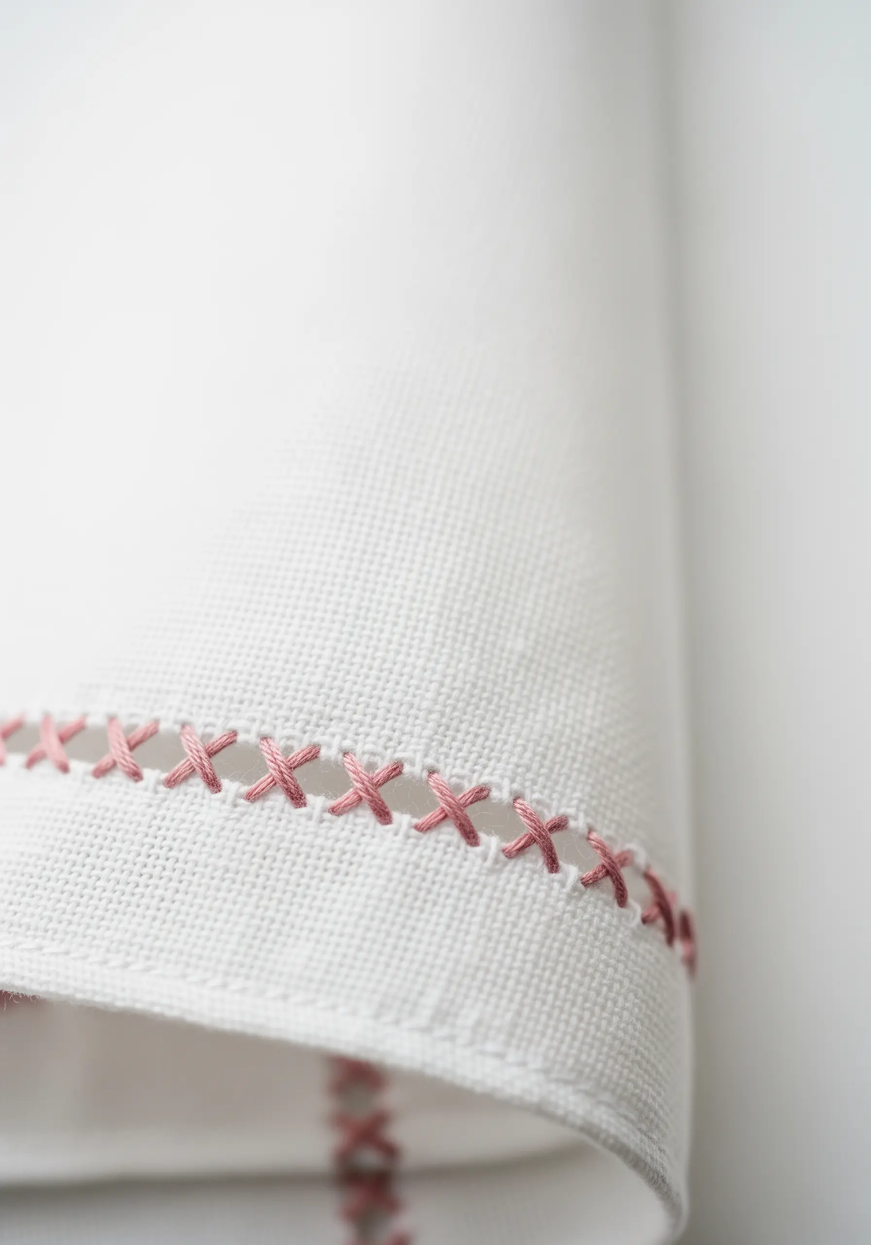 Close-up of a pink cross-stitch or hemstitch detail along the folded edge of a white linen handkerchief.