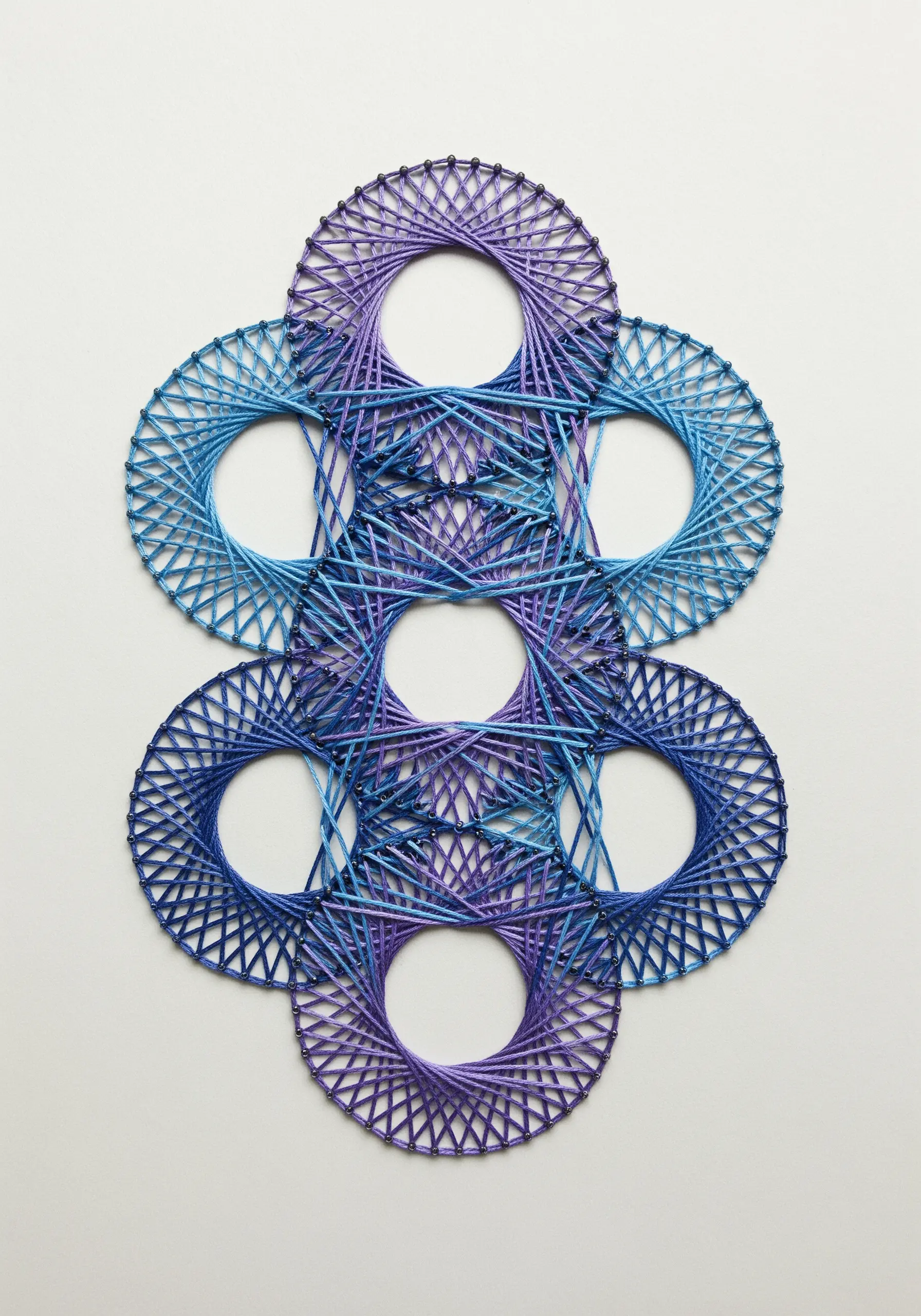Geometric string art embroidery with blue and purple thread wrapped around circular forms.