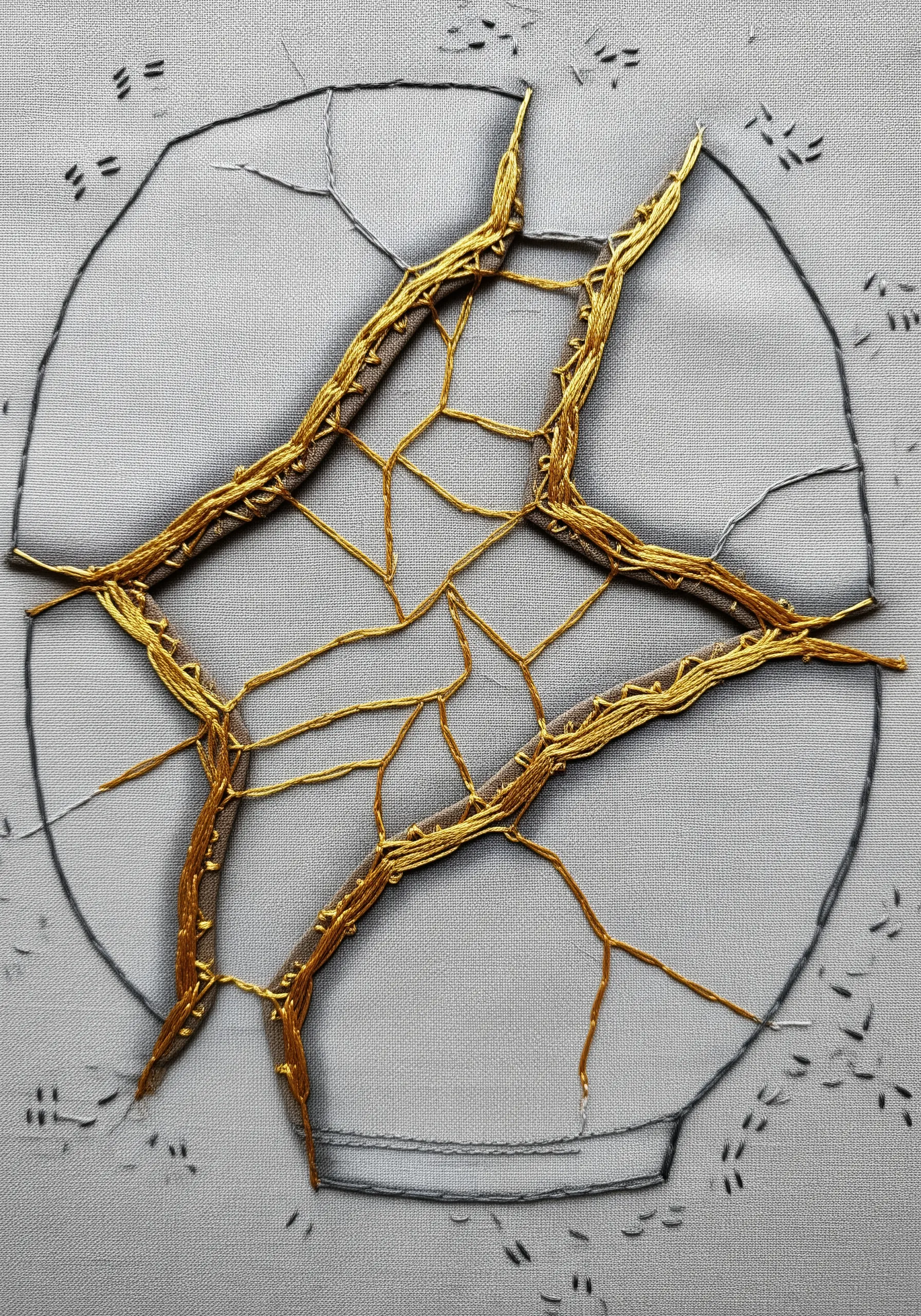 Embroidery inspired by Kintsugi, with gold thread mending cracks on grey fabric.
